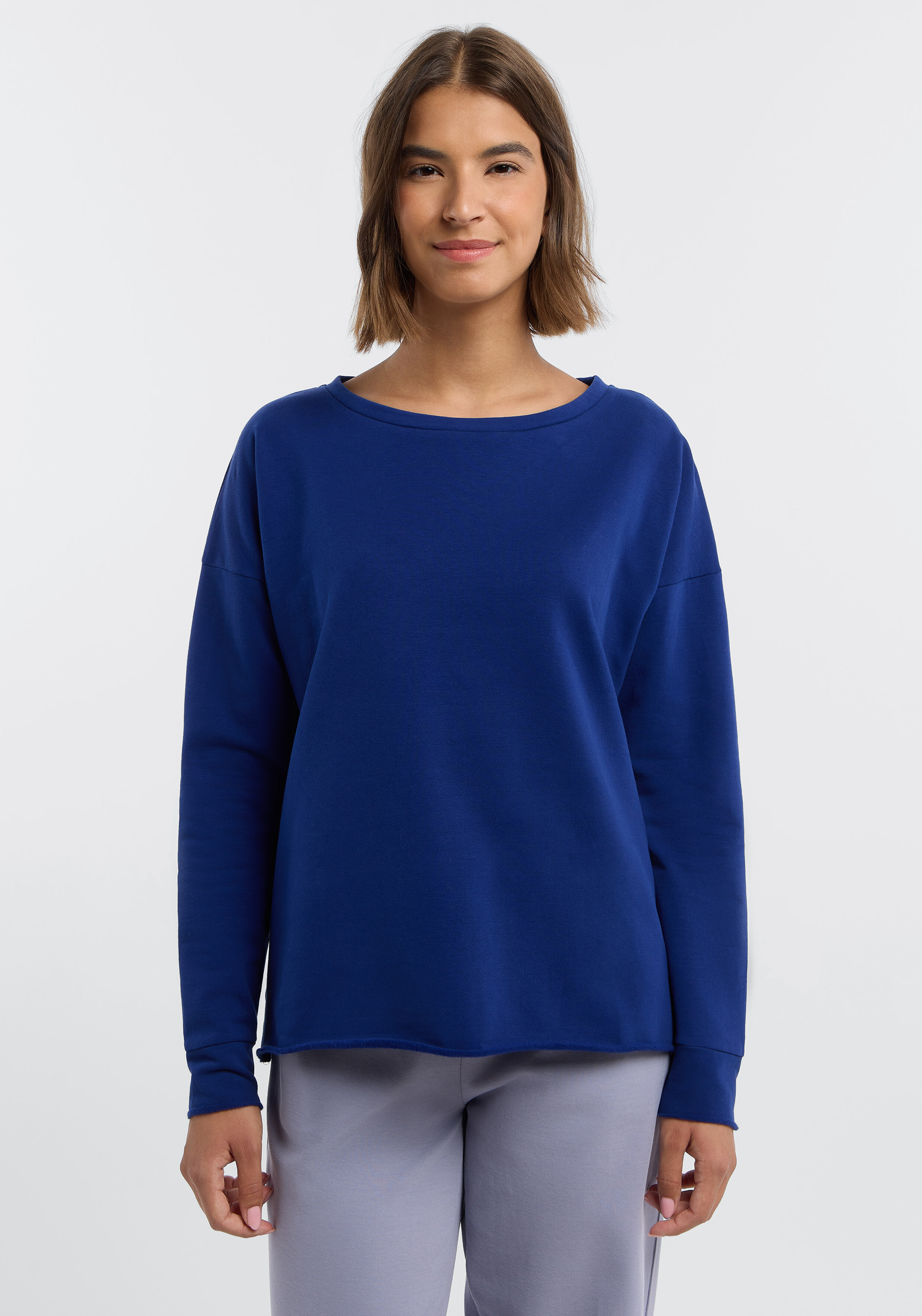 Frau trägt ein gemütliches, königsblaues, langärmliges Freizeit-Sweatshirt mit offenem Saum.