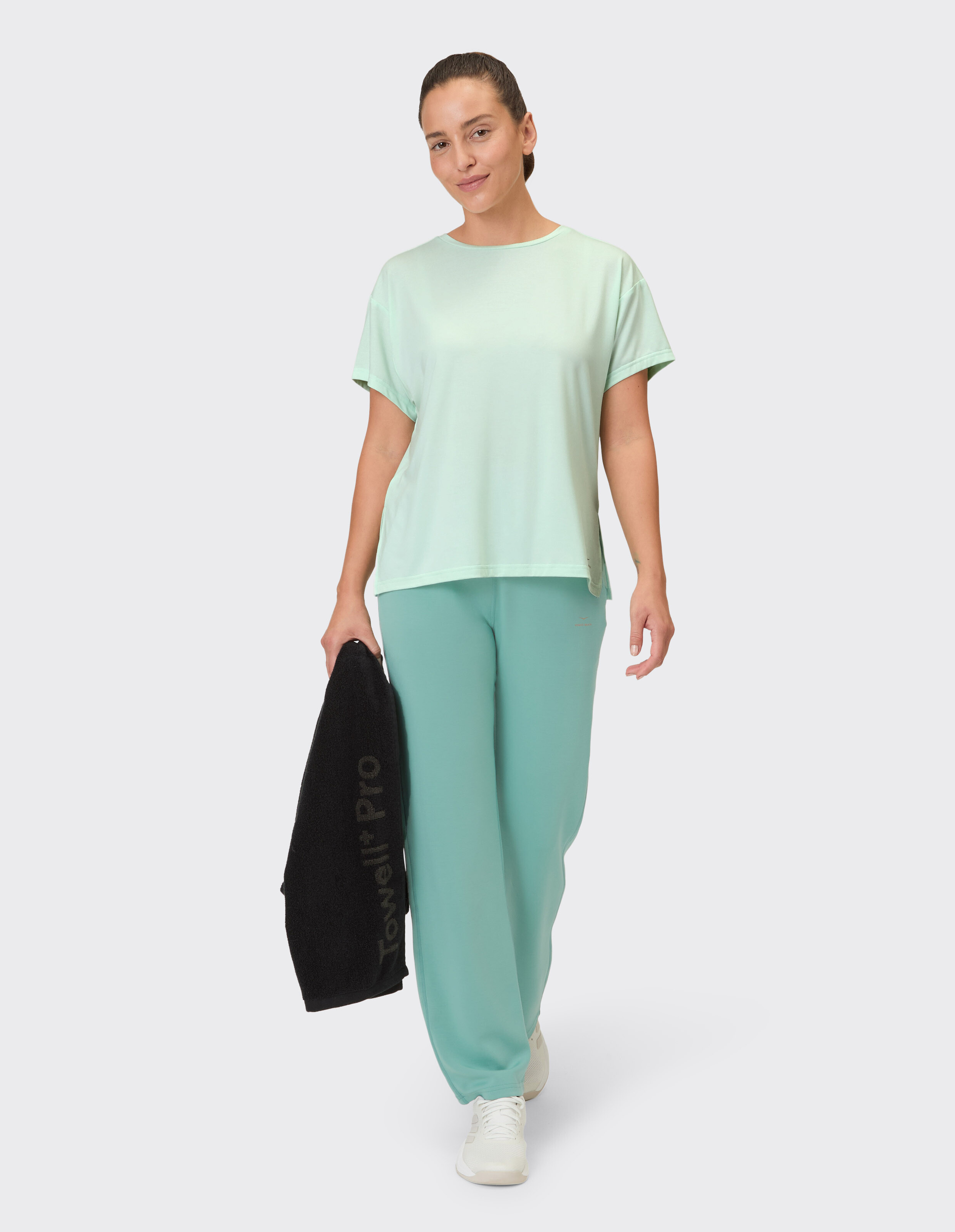 Frau in mintgrünem Freizeit-T-Shirt und passender Lounge-Hose mit schwarzem Handtuch.