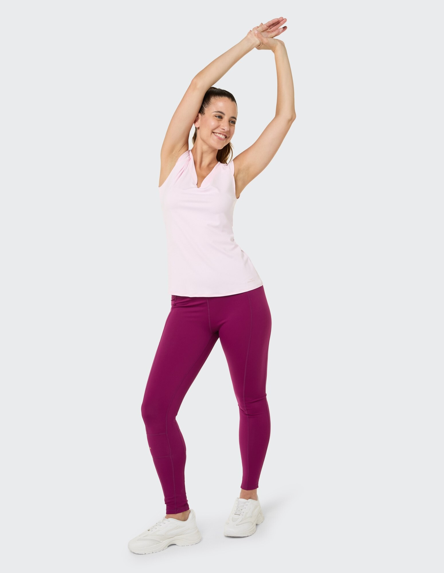 Frau in einem rosa ärmellosen Top und lila Leggings präsentiert lässige Aktivkleidung.