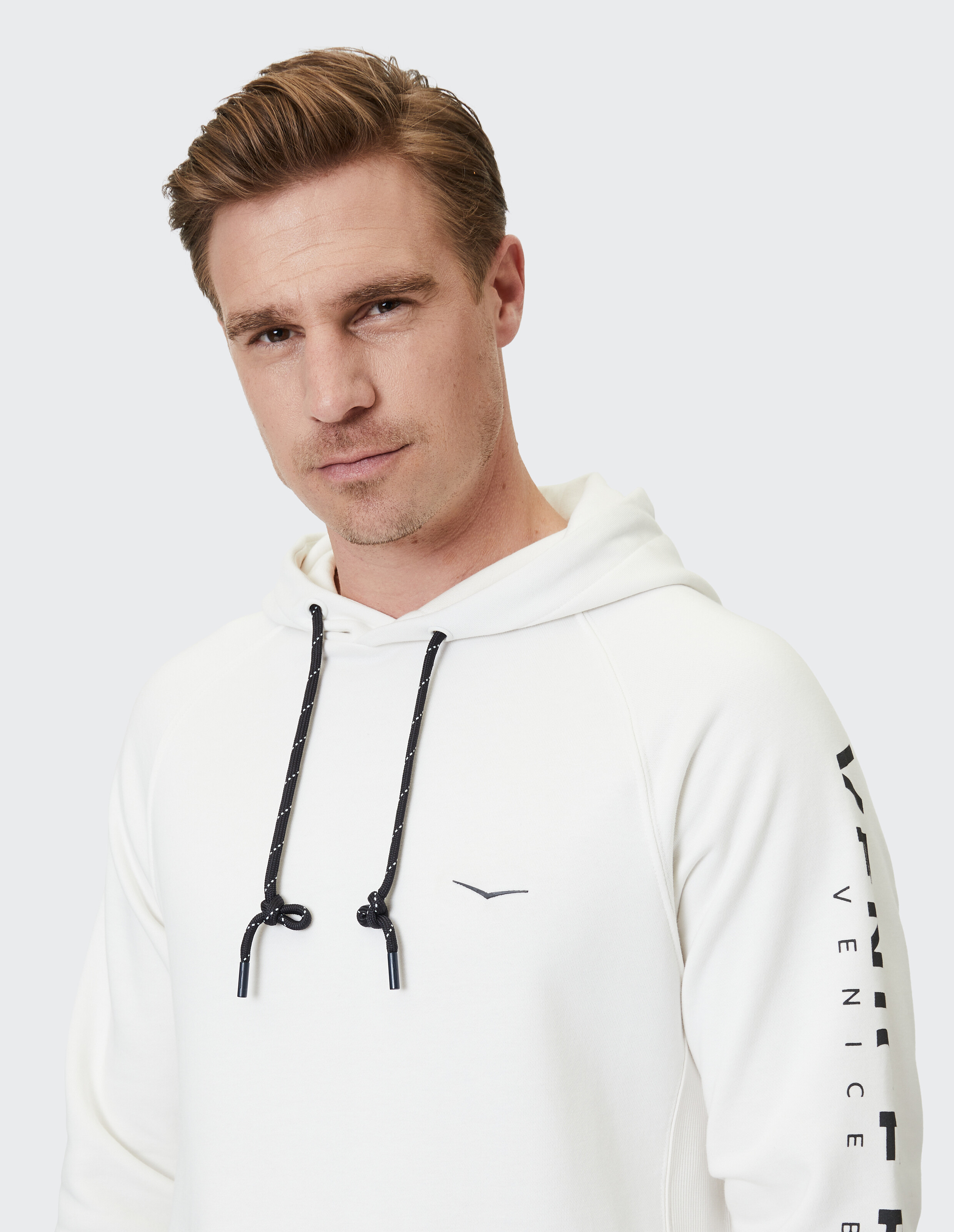 Mann trägt einen weißen ELBSAND-Freizeit-Kapuzenpullover mit schwarzen Kordelzügen und Logo-Aufdruck am Ärmel.