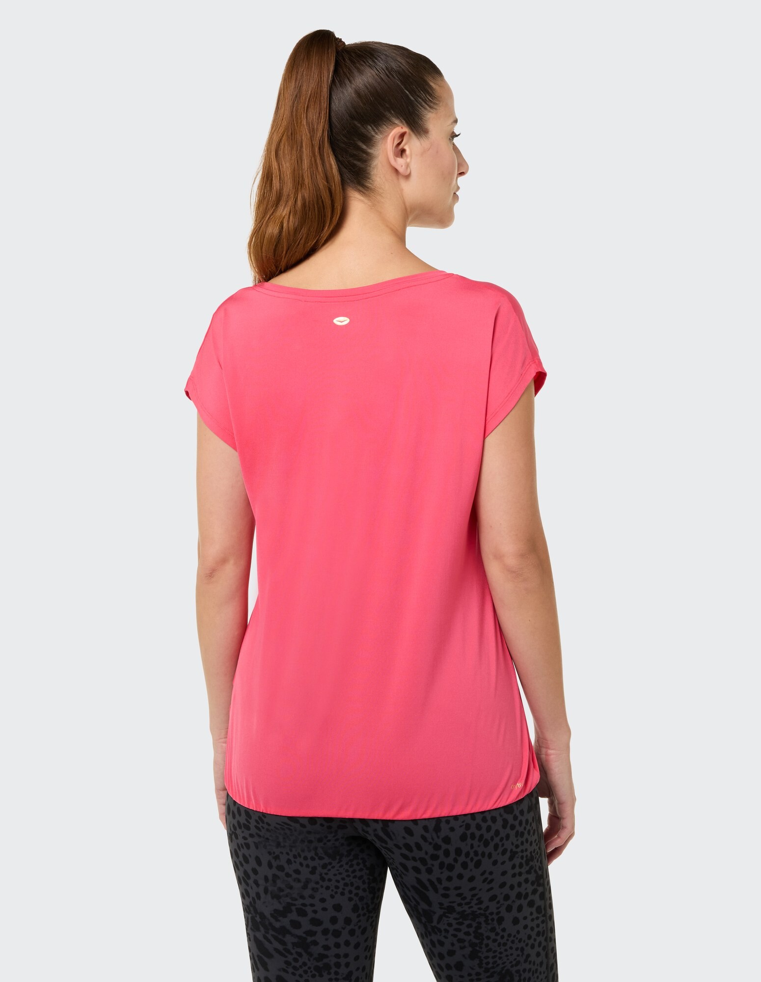 Rückansicht einer Frau in einem rosa Freizeitoberteil und schwarzen Leggings mit Leopardenmuster.