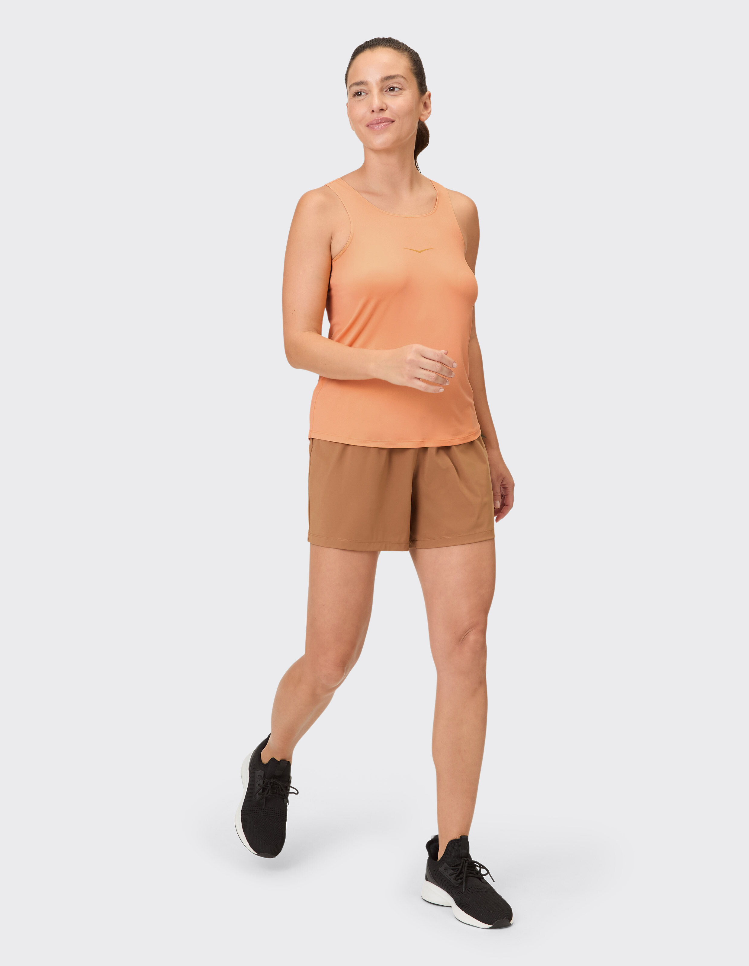 Frau trägt ein orangefarbenes Tanktop und braune Shorts für einen lässigen, sportlichen Stil.