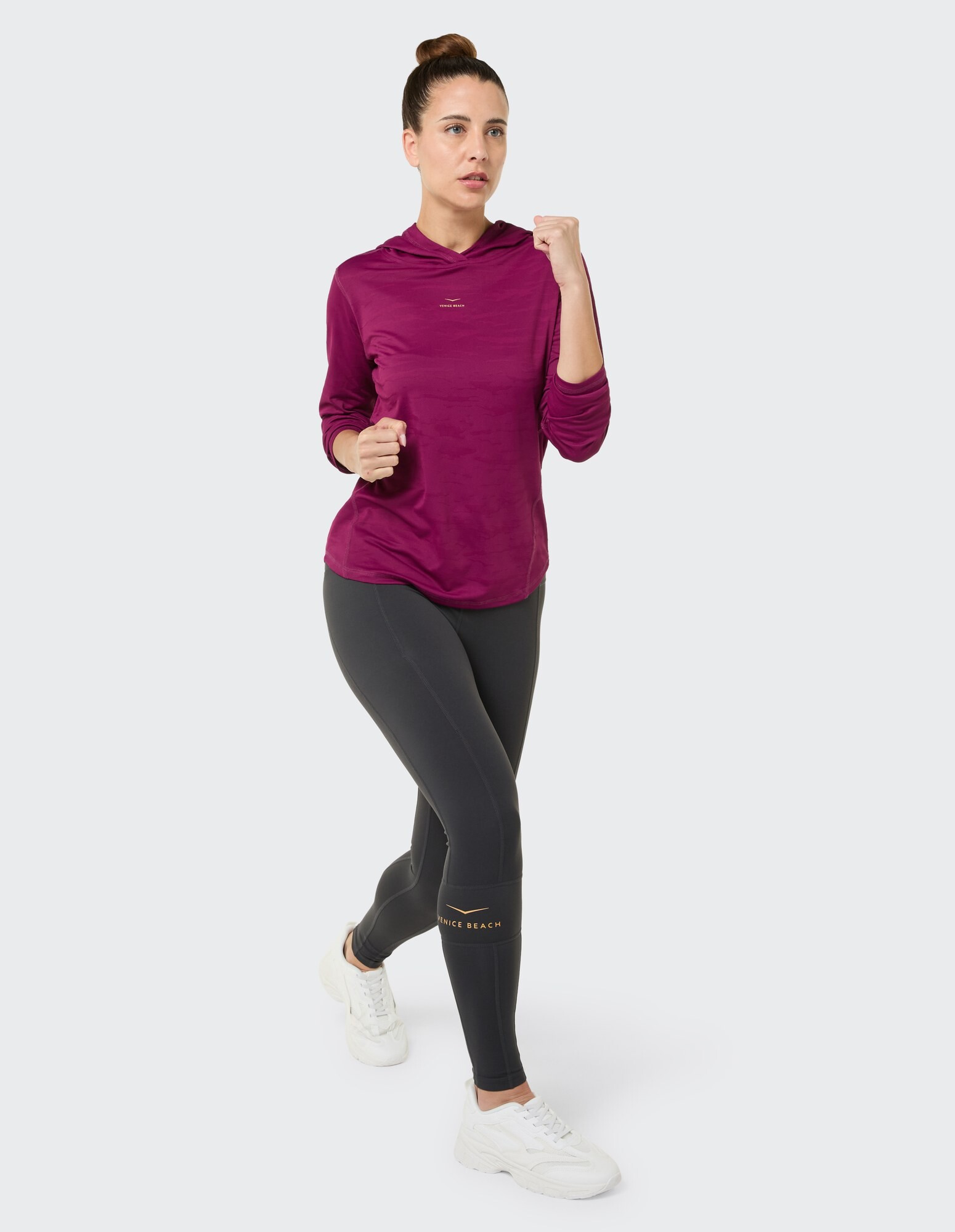 Frau in einem lila Kapuzenpullover und schwarzen Leggings, die in lässiger Sportkleidung unterwegs ist.