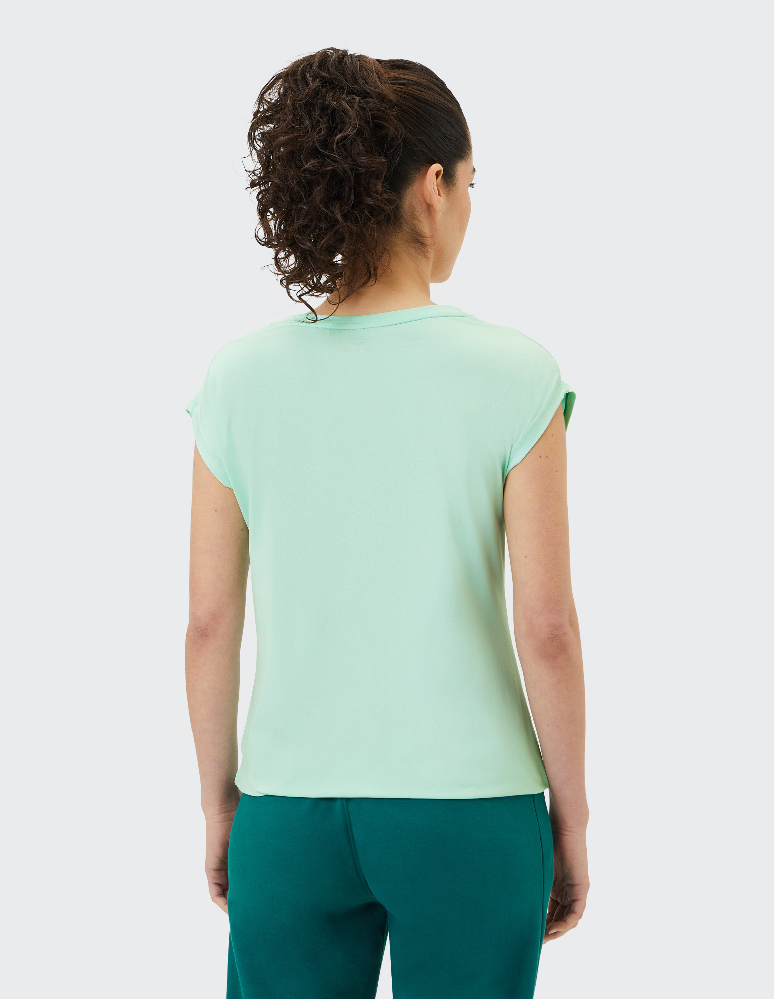 Rückansicht einer Frau, die ein hellgrünes Freizeit-T-Shirt und eine dunkelgrüne Lounge-Hose trägt.
