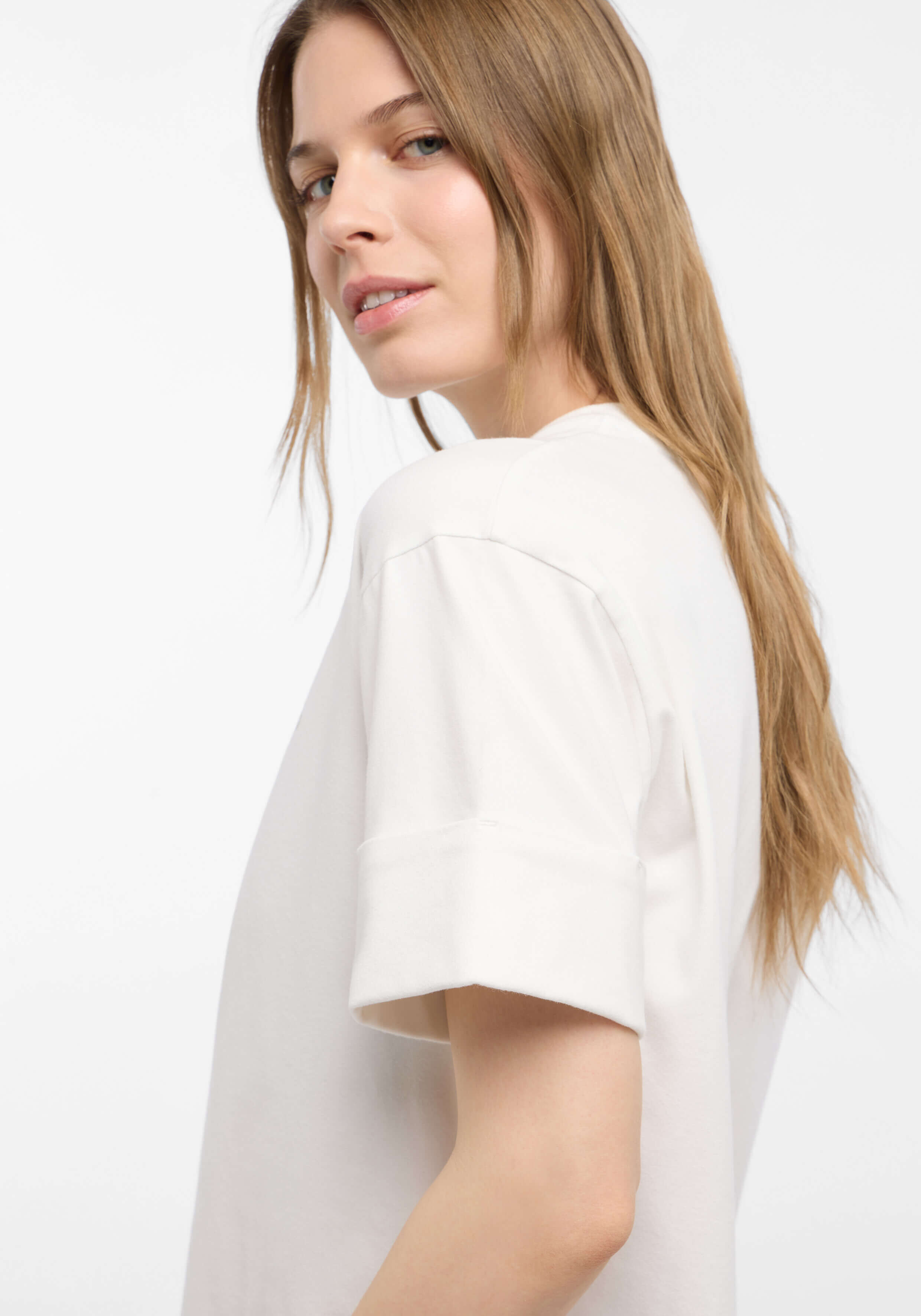 Frau trägt ein gemütliches weißes Freizeit-T-Shirt mit Bündchen an den Ärmeln, perfekt zum Entspannen.