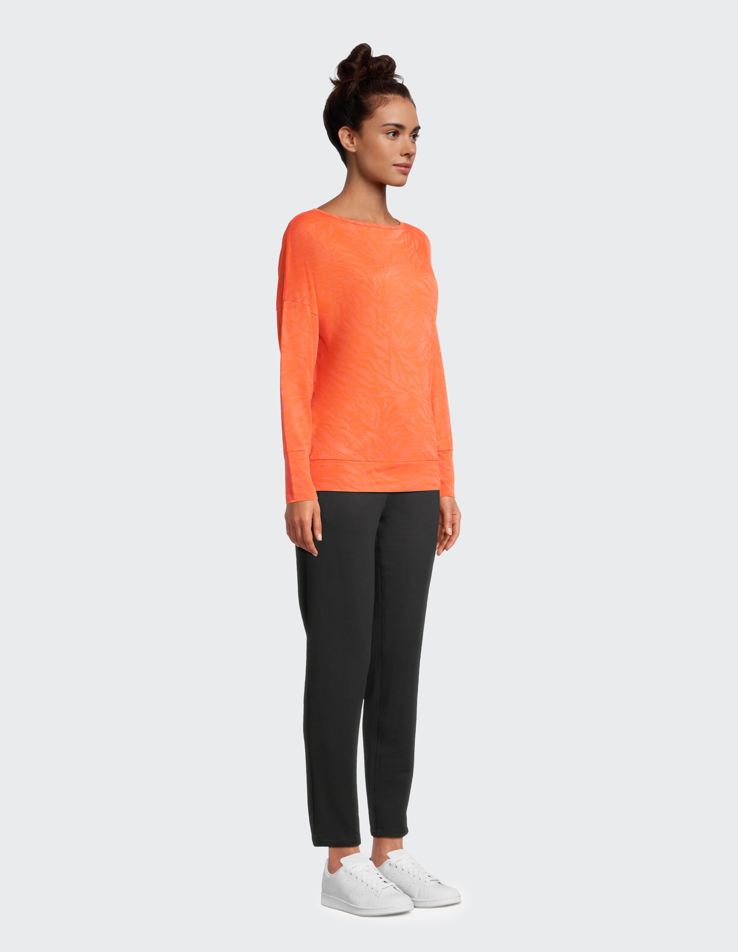 Frau trägt ein orangefarbenes Venice Beach Langarmshirt Calma mit schwarzer Hose.