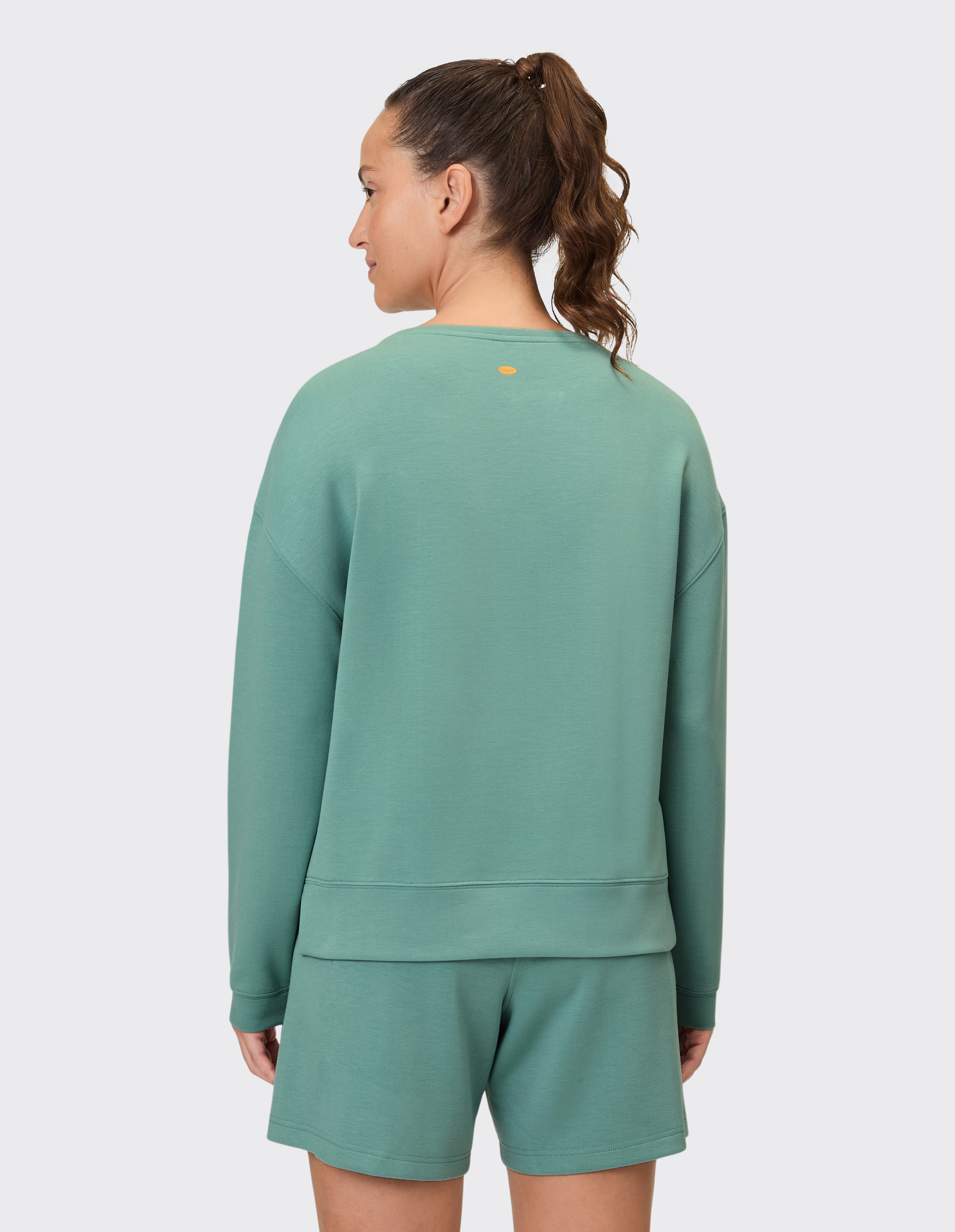 Rückansicht einer Frau in einem grünen, lässigen Sweatshirt und Shorts.