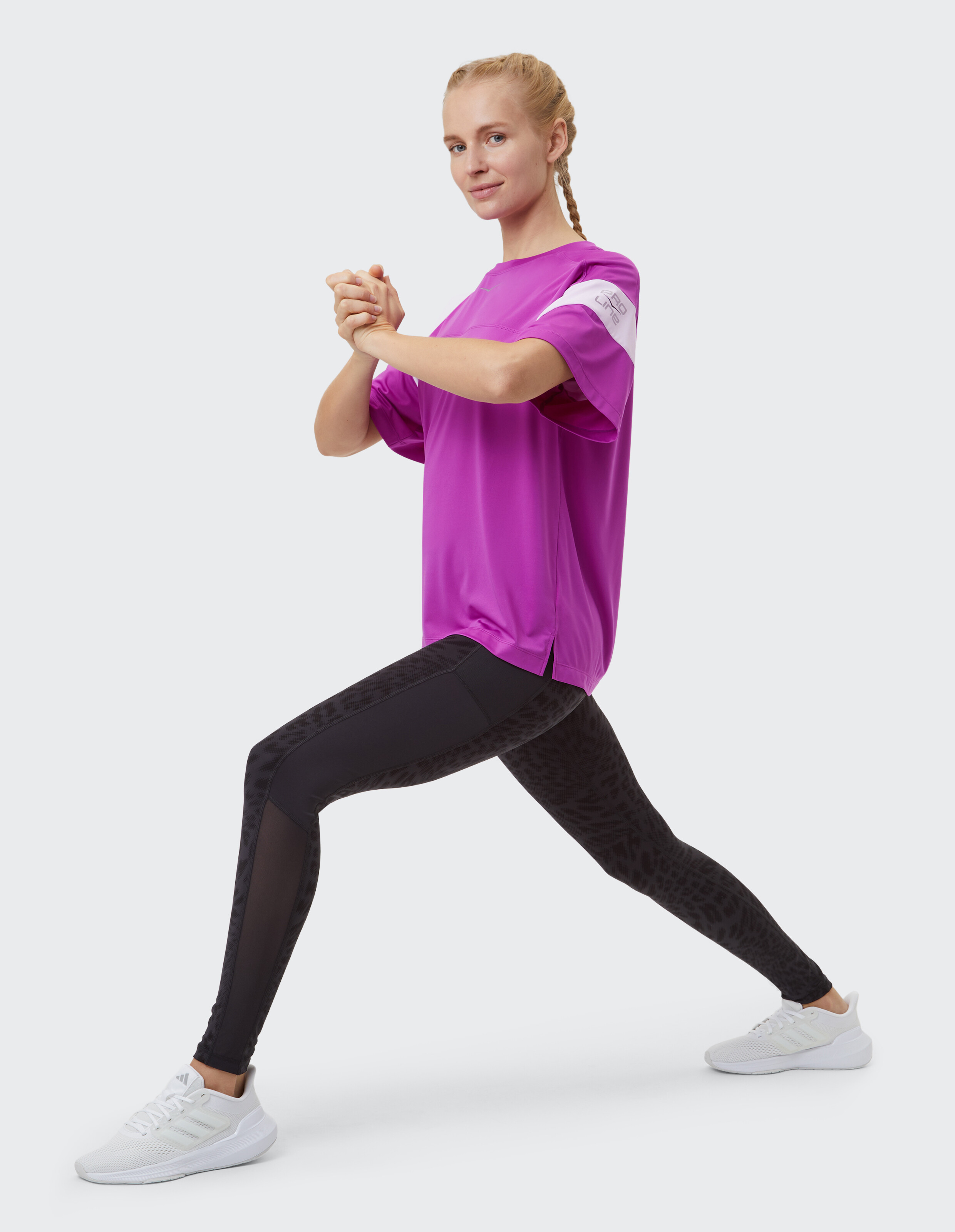 Frau in lila T-Shirt und schwarz gemusterten Leggings macht einen Ausfallschritt.