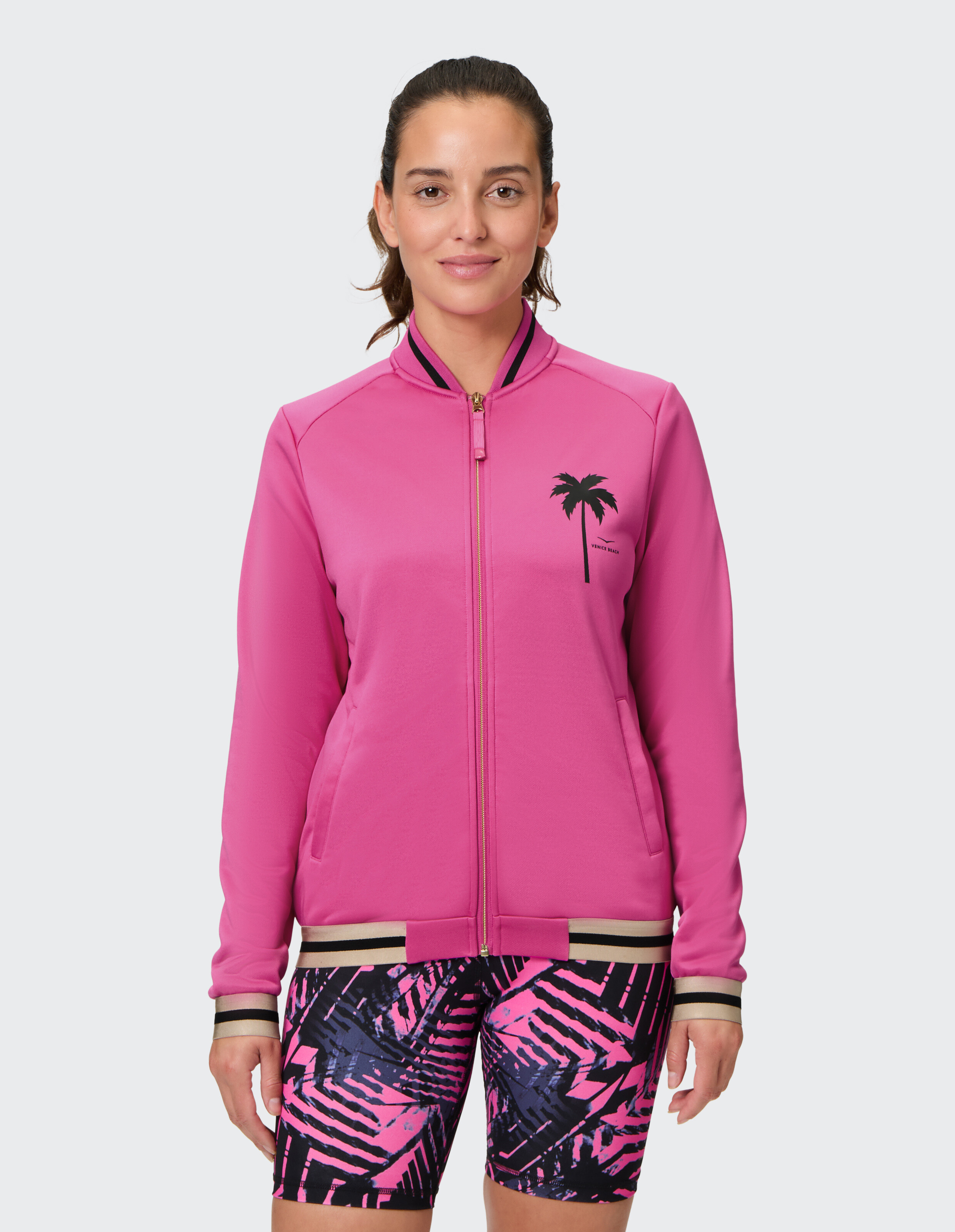 Frau in einer rosafarbenen Reißverschlussjacke mit Palmenmuster und gemusterten Shorts.
