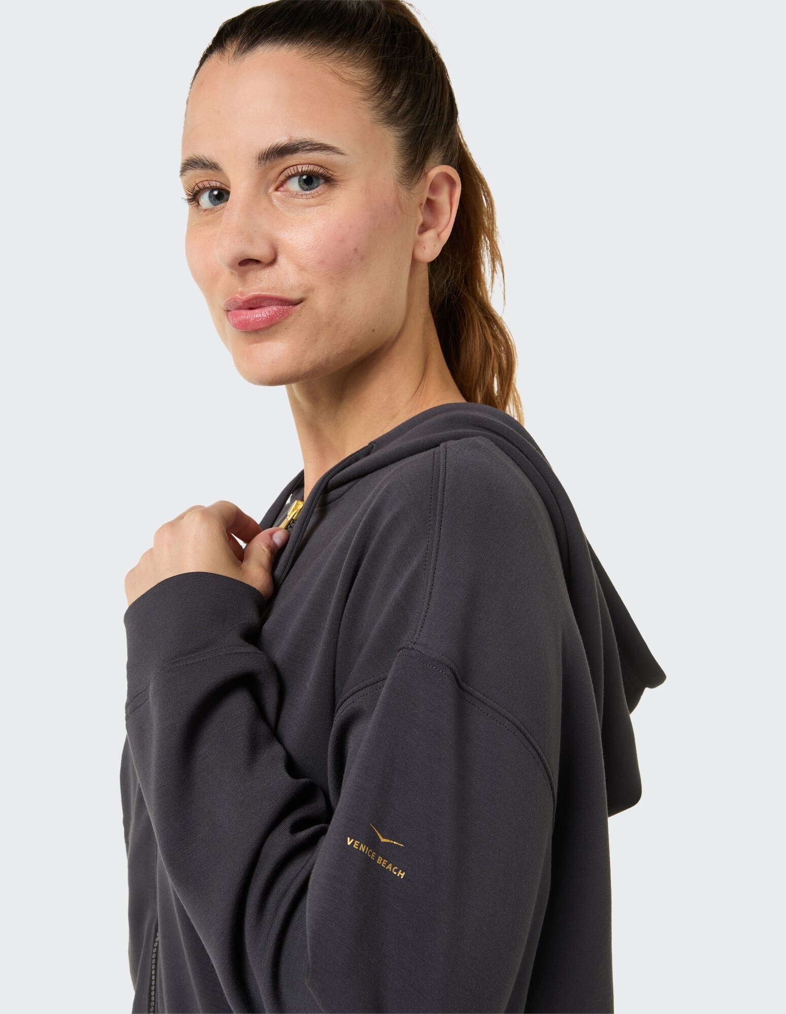Frau in einem dunkelgrauen Kapuzenpullover mit goldenem Logo, der lässigen Stil und Komfort unterstreicht.