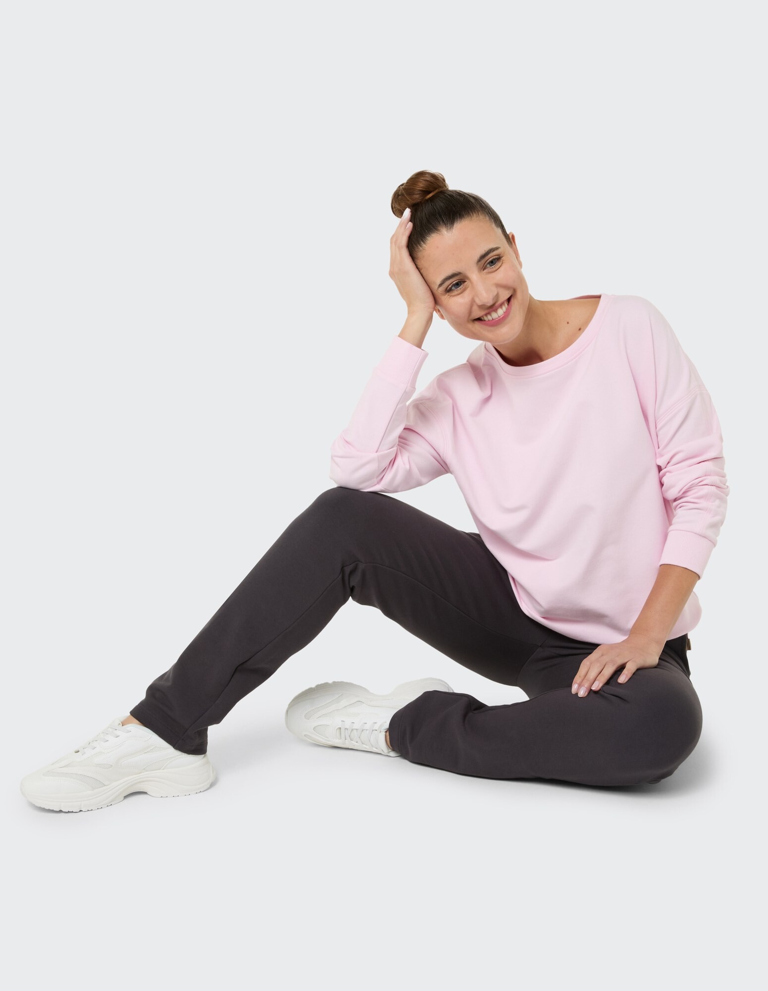 Frau in rosa Sweatshirt und dunkler Hose sitzt lässig in stylischen Sneakers.