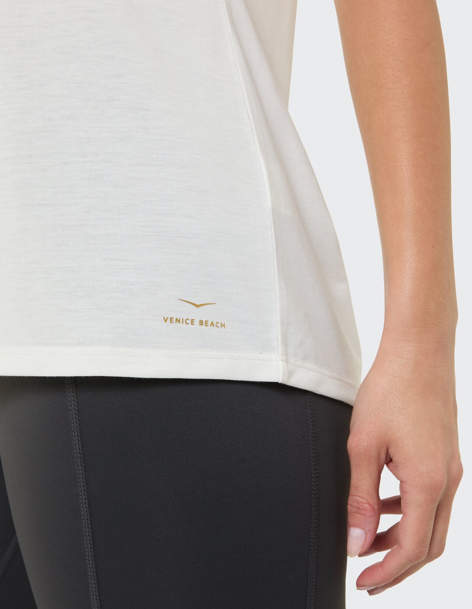 Nahaufnahme eines hellcremefarbenen Oberteils mit „Venice Beach“-Logo und schwarzen Leggings.