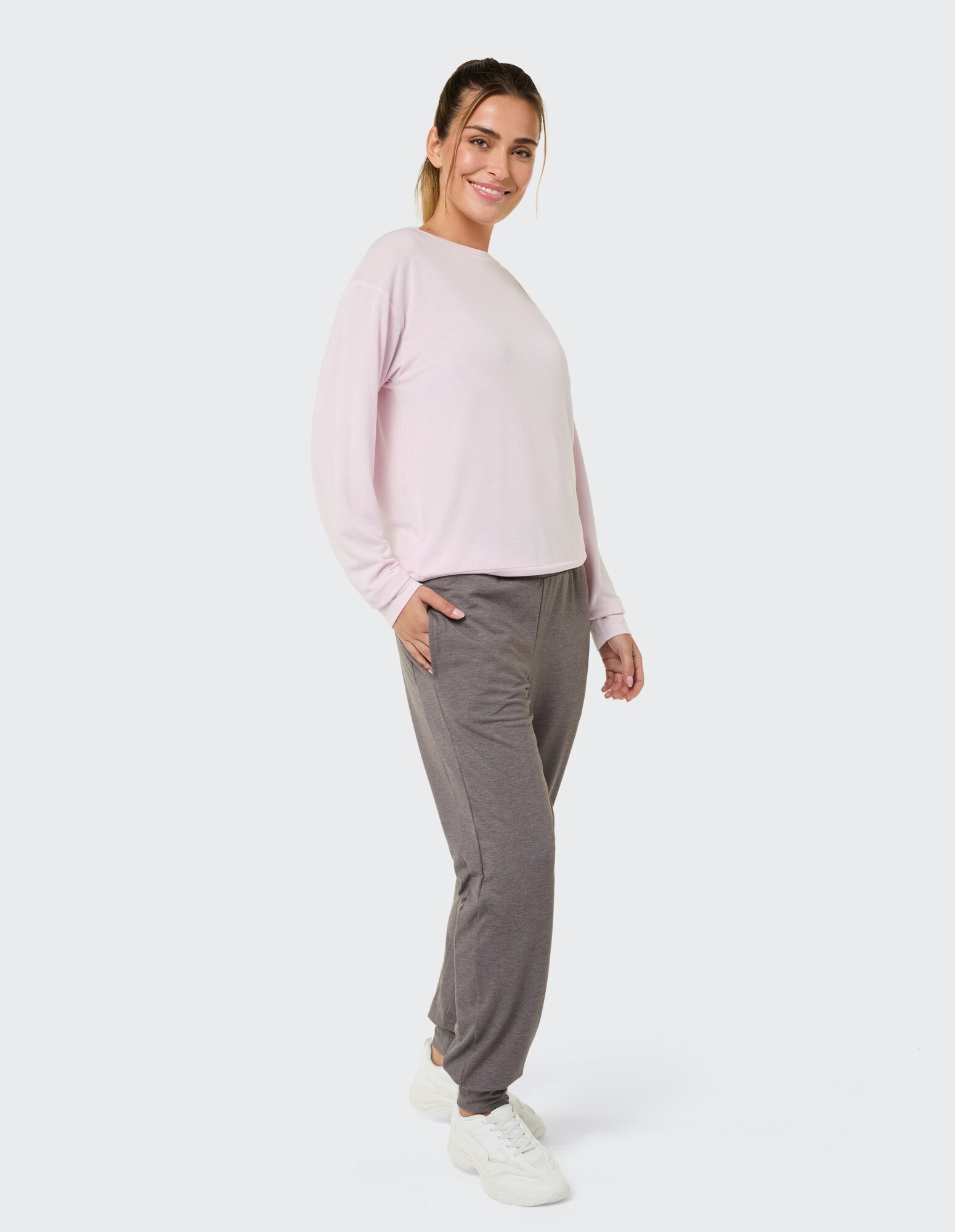 Frau in hellrosa Langarmshirt und grauer Jogginghose lächelt lässig.