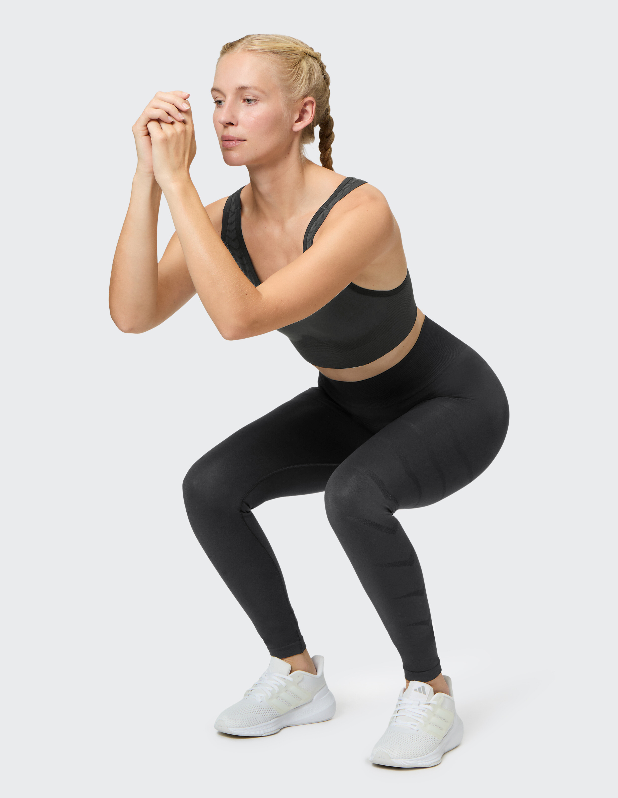 Frau in schwarzem nahtlosem Sport-BH und Leggings führt eine Kniebeugenübung durch.
