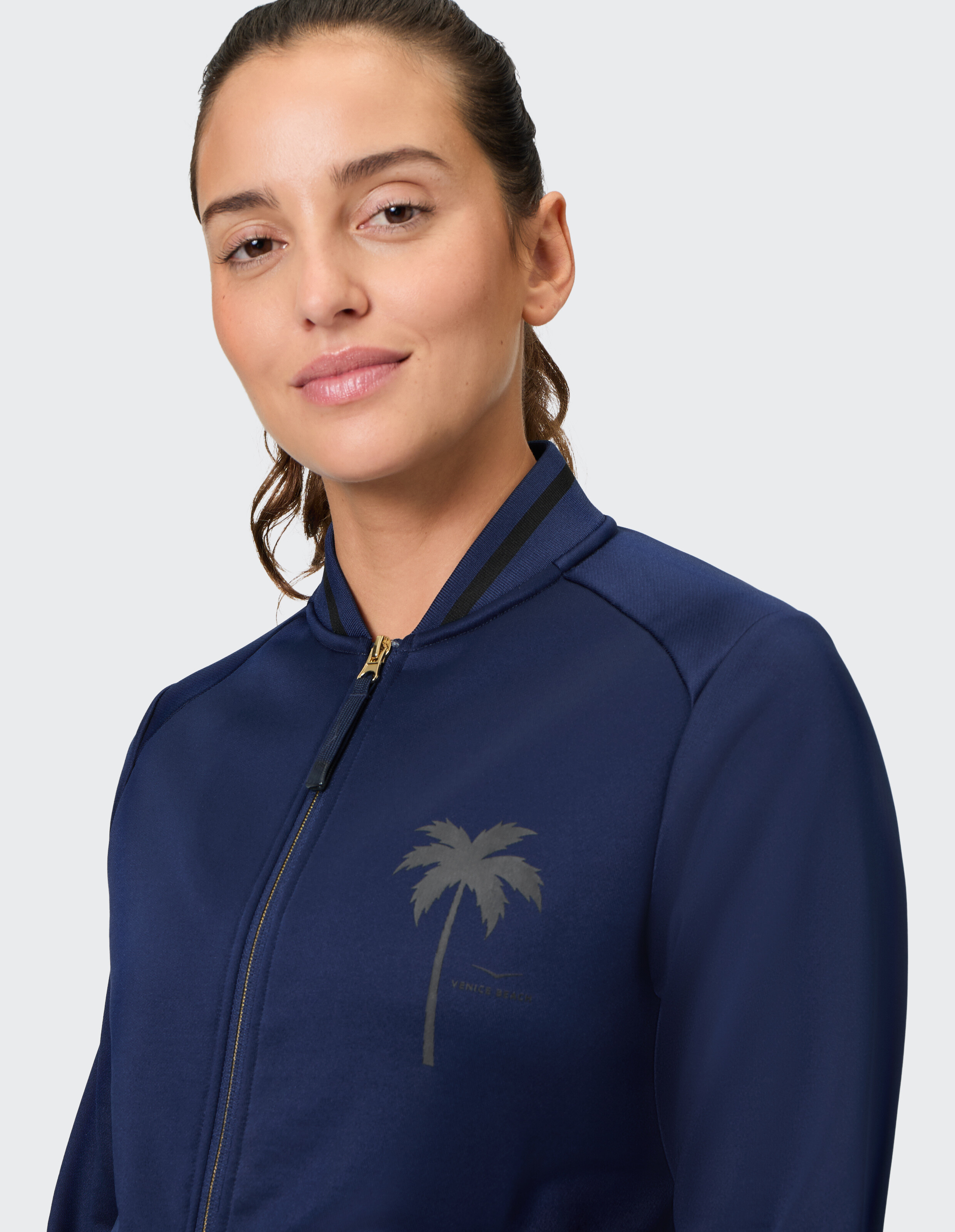 Frau trägt eine marineblaue Bomberjacke mit Reißverschluss und Palmenprint.