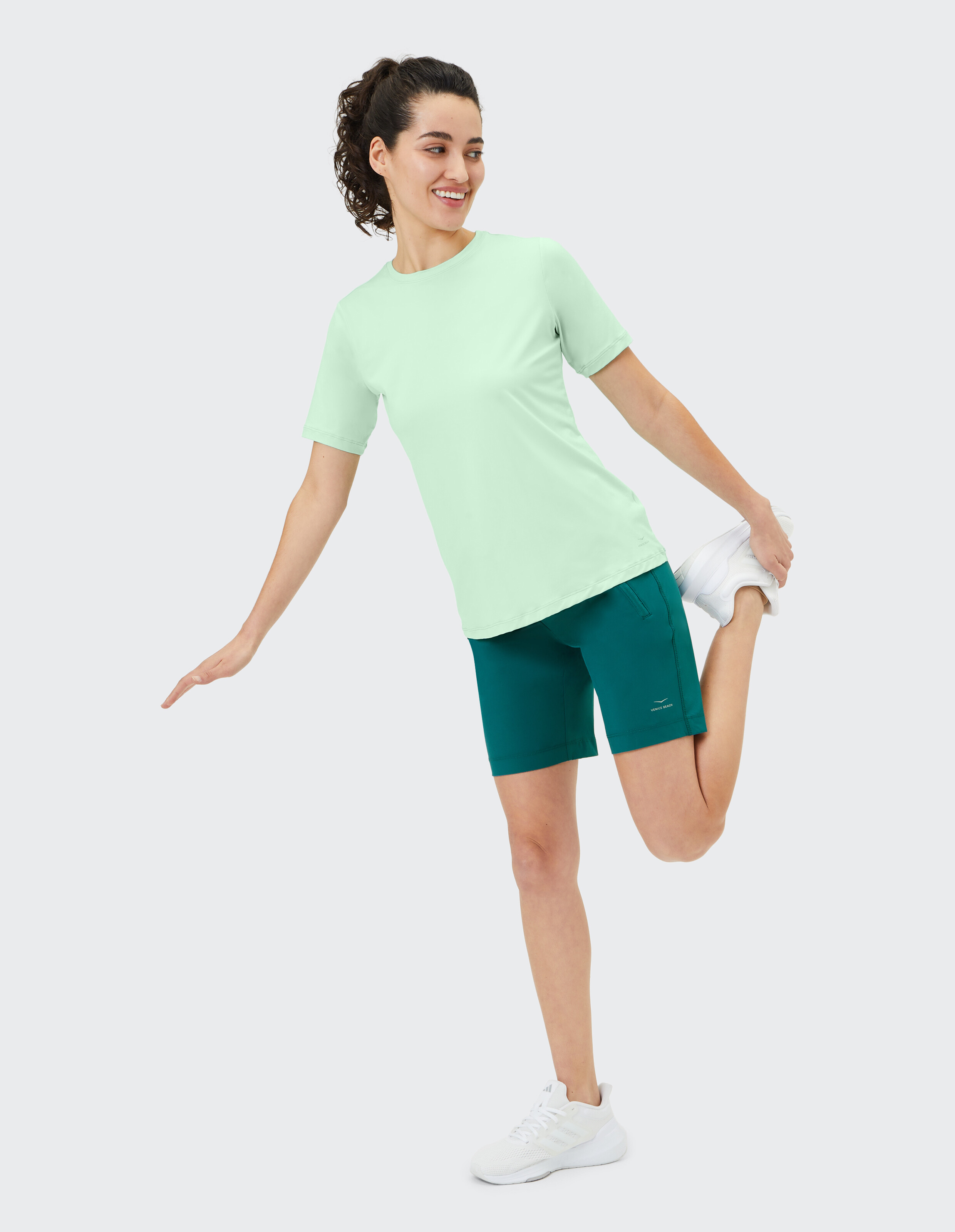 Frau in mintgrünem T-Shirt und blaugrünen Shorts im lässigen Activewear-Stil.