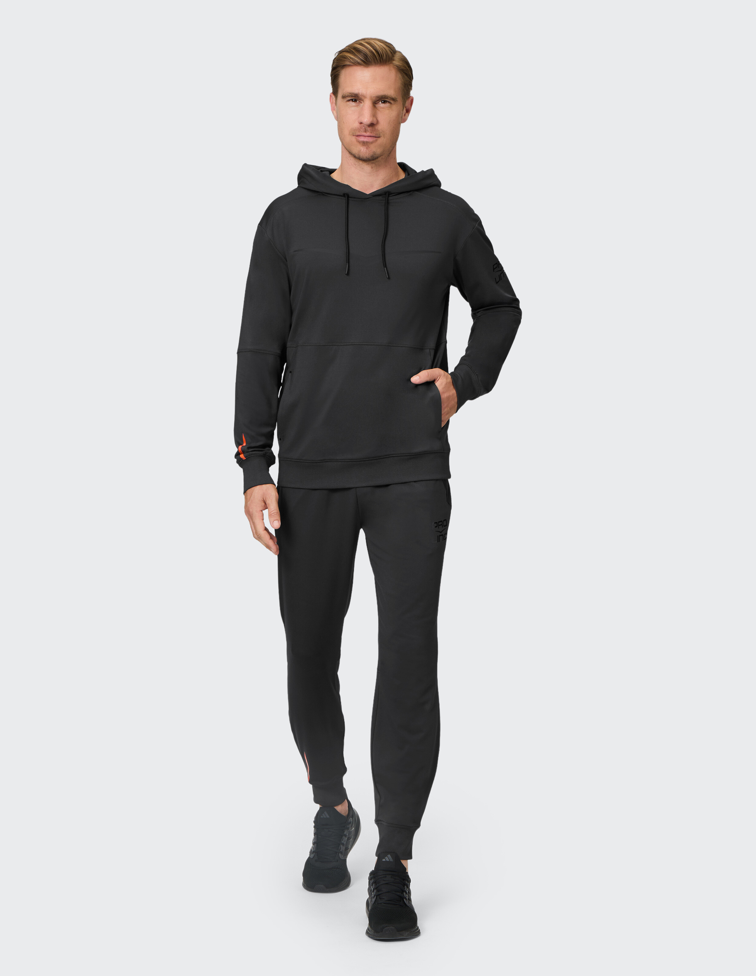 Mann mit schwarzem Kapuzenpullover und passender Jogginghose, ideal für Freizeitkleidung.