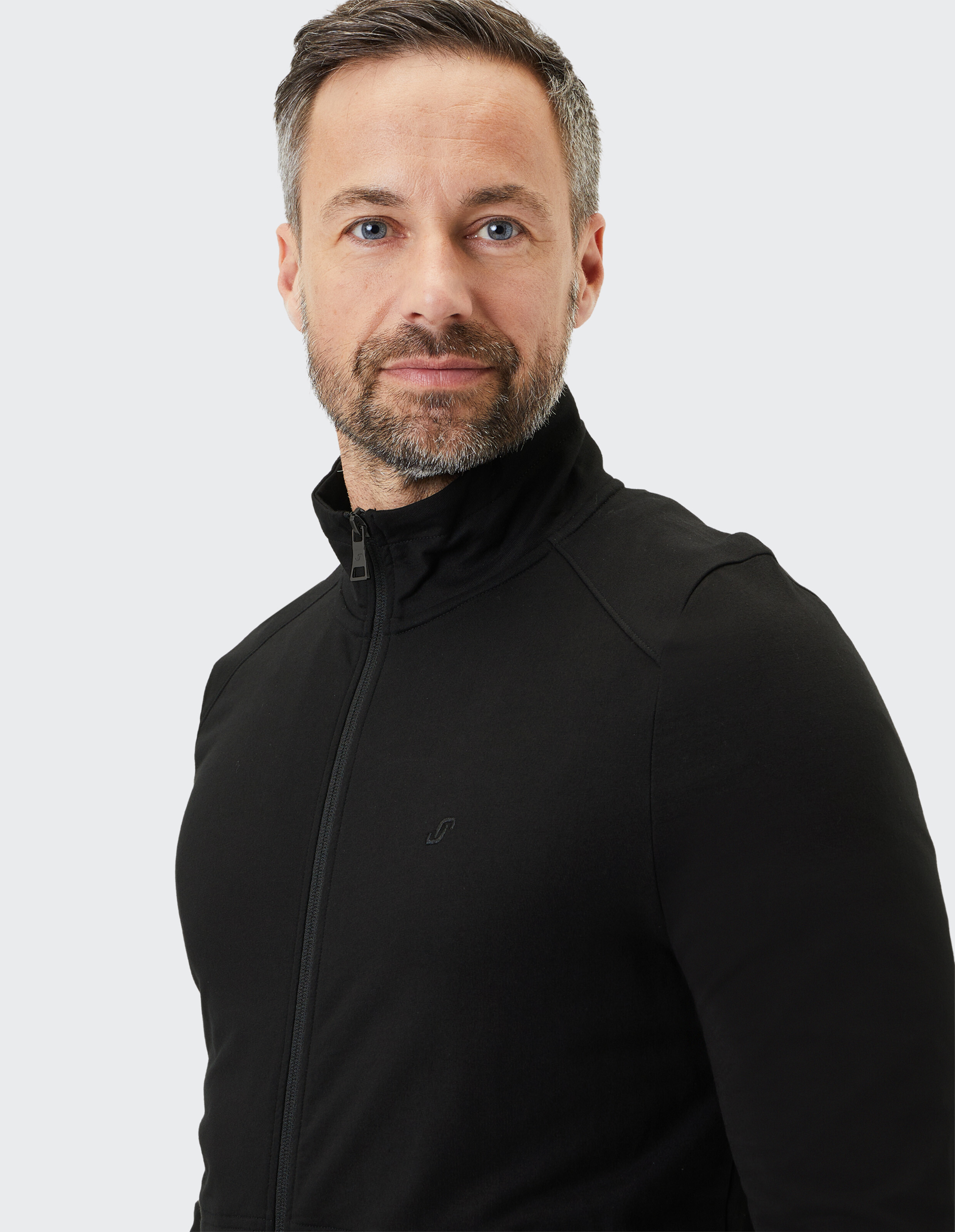 Ein Mann mit Bart, grauem Haar und schwarzem Rollkragenpullover blickt freundlich in die Kamera, vor grauem Hintergrund.