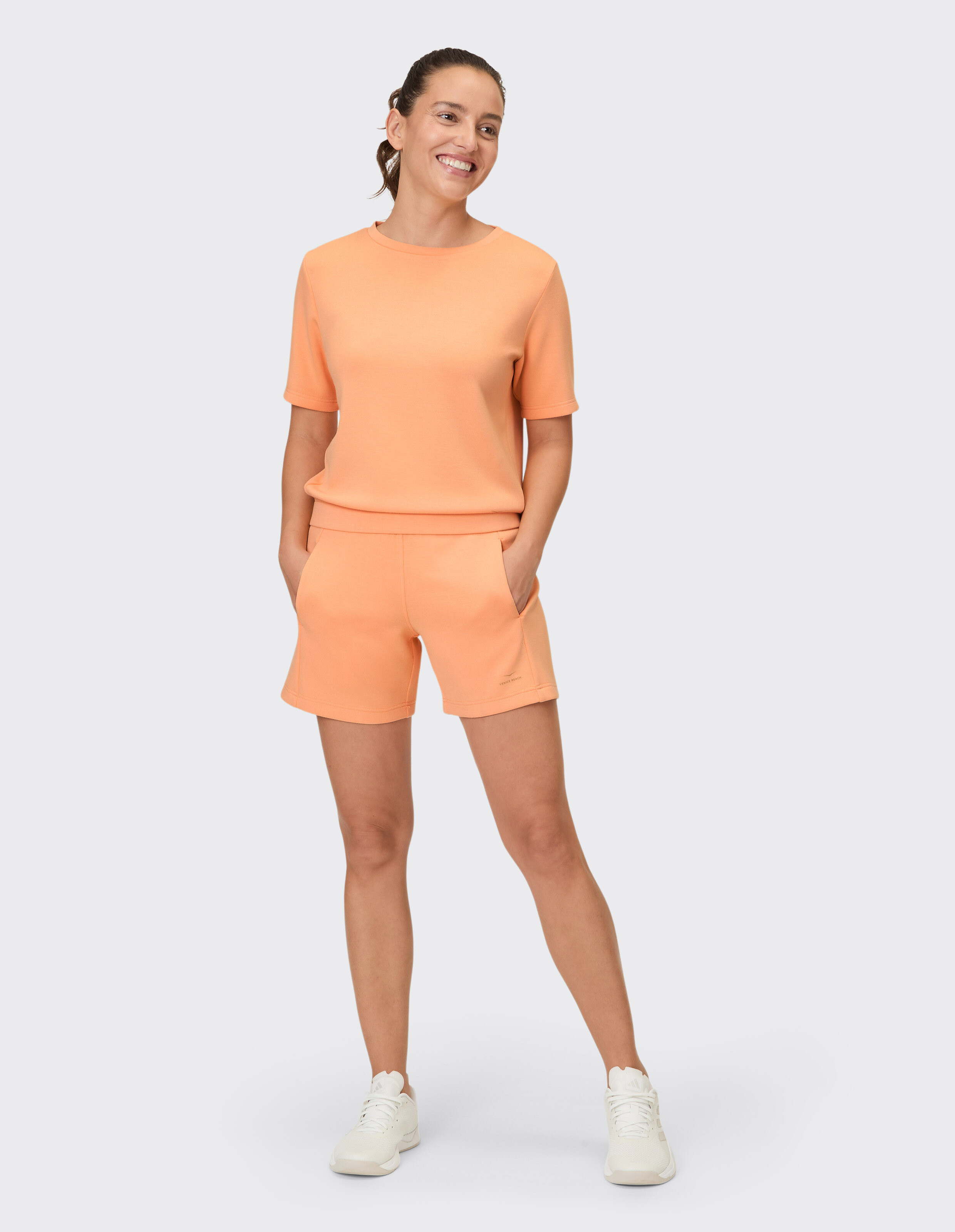 Frau in pfirsichfarbenem, lässigem Set bestehend aus einem kurzärmeligen Oberteil und Shorts, perfekt zum Entspannen.