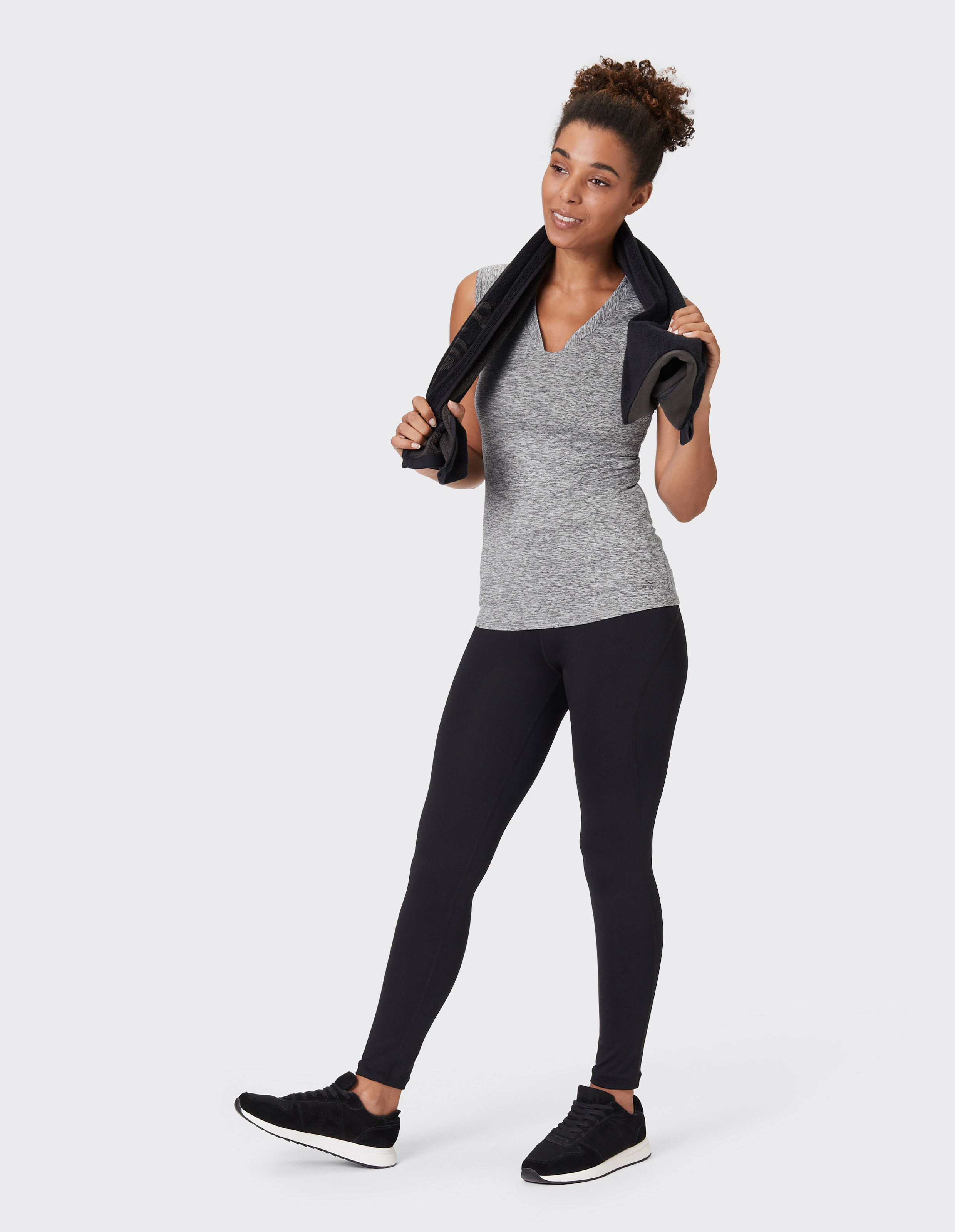 Frau in einem grauen Tanktop mit V-Ausschnitt und schwarzen Leggings mit Handtuch, perfekt für lässige Aktivkleidung.