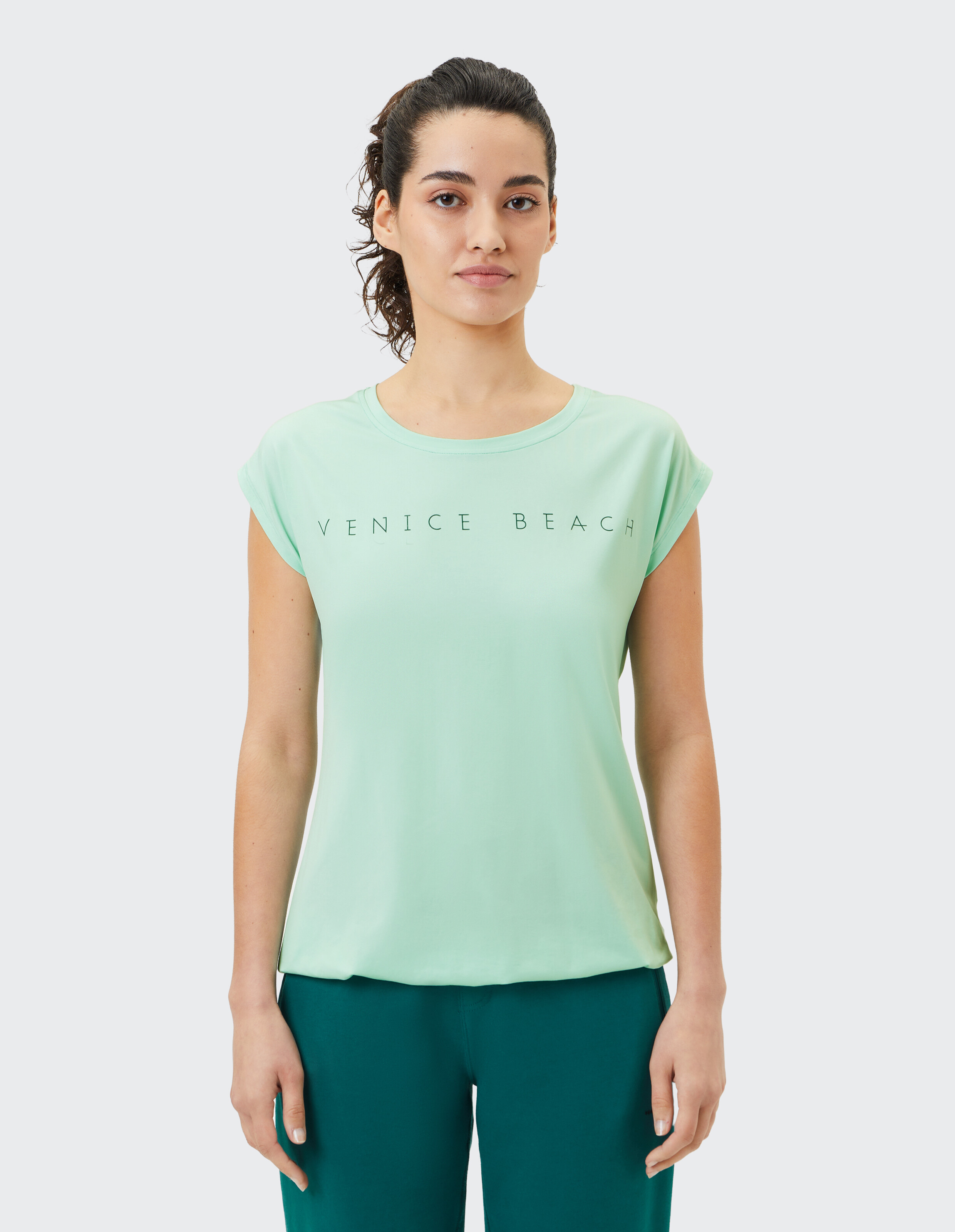 Frau trägt ein hellgrünes lässiges Venice Beach-T-Shirt zum Faulenzen.
