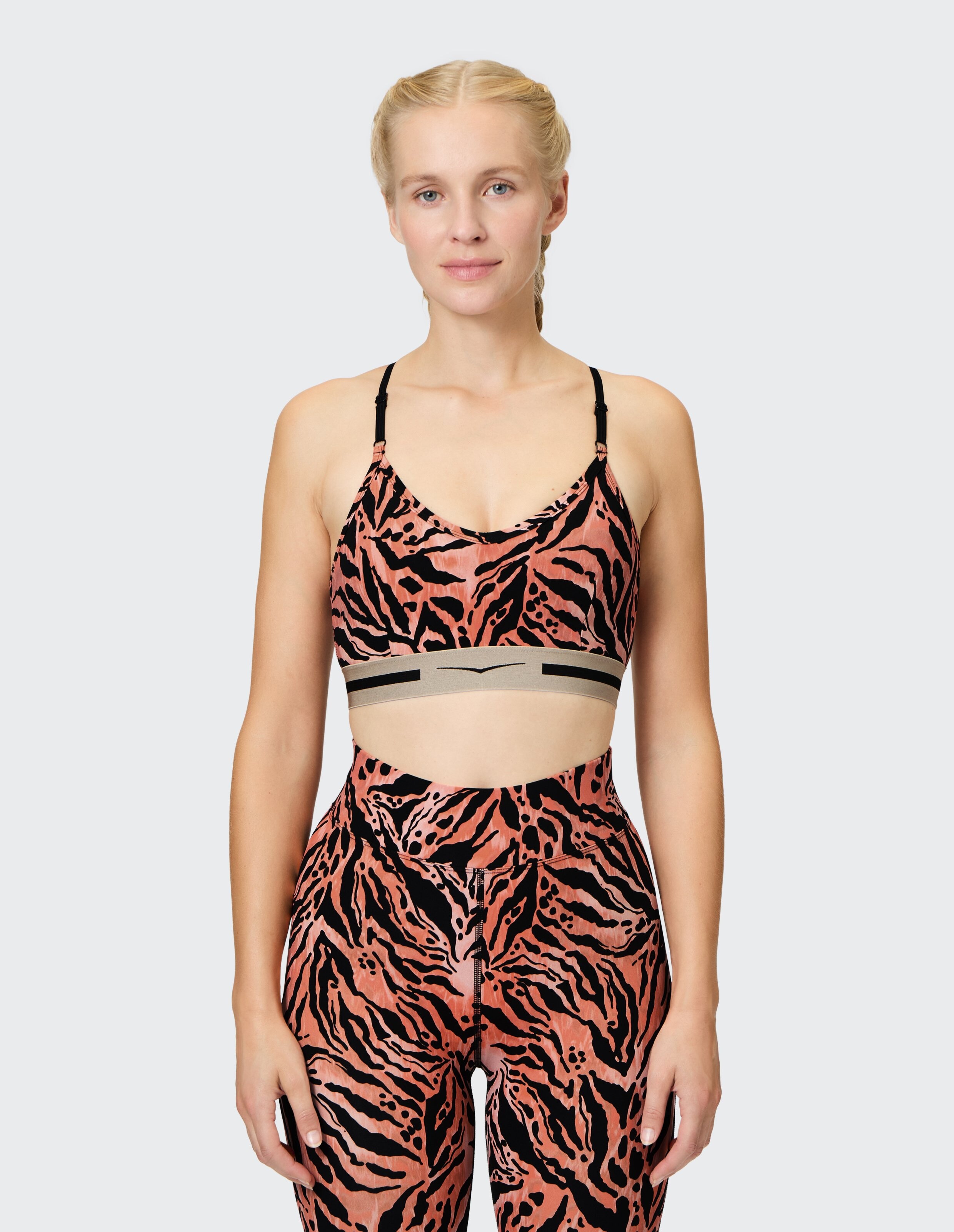 Frau trägt einen Sport-BH mit Korallen- und schwarzem Tigermuster und passende Leggings.