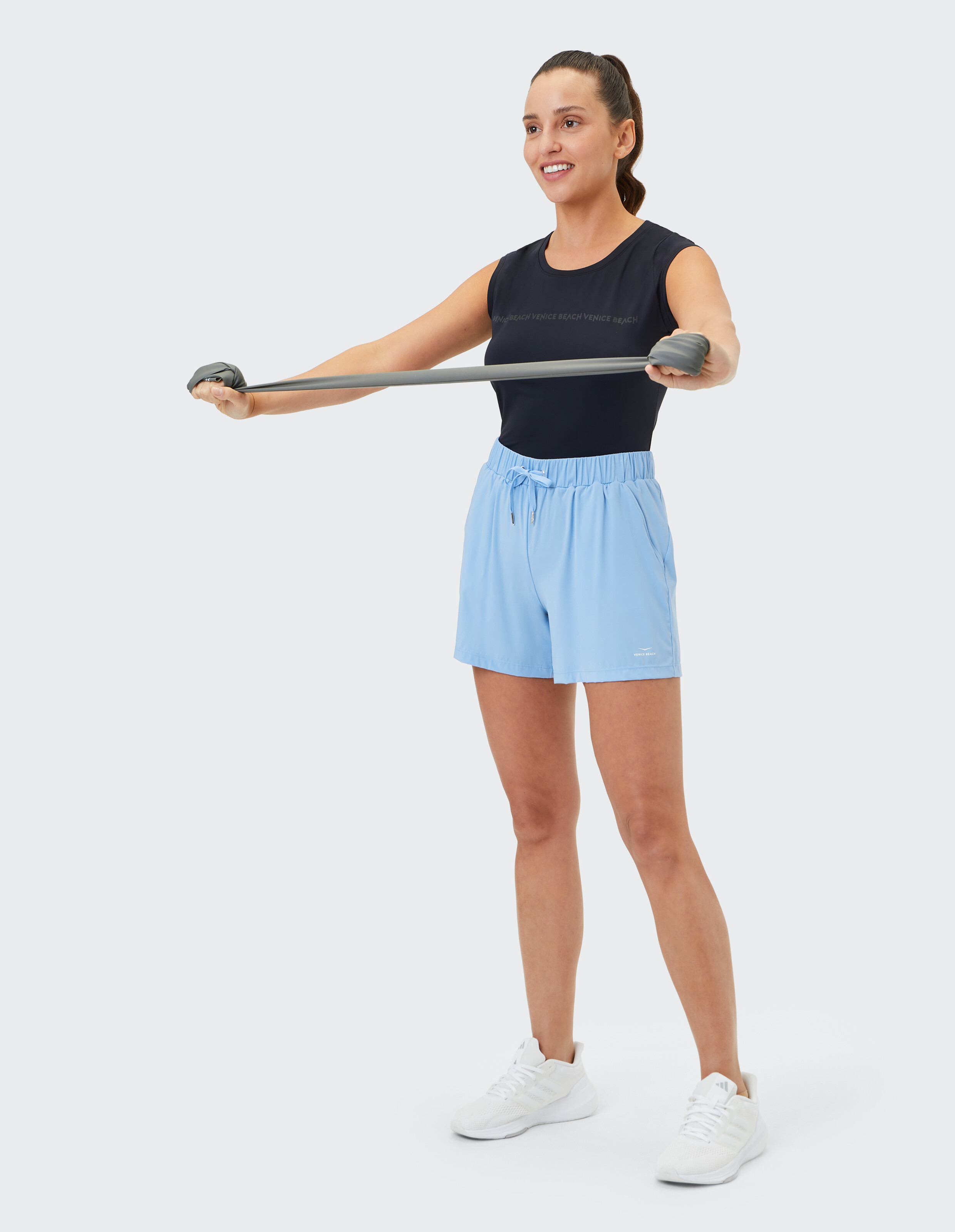 Frau in schwarzem Tanktop und hellblauen Shorts trainiert mit einem Widerstandsband.