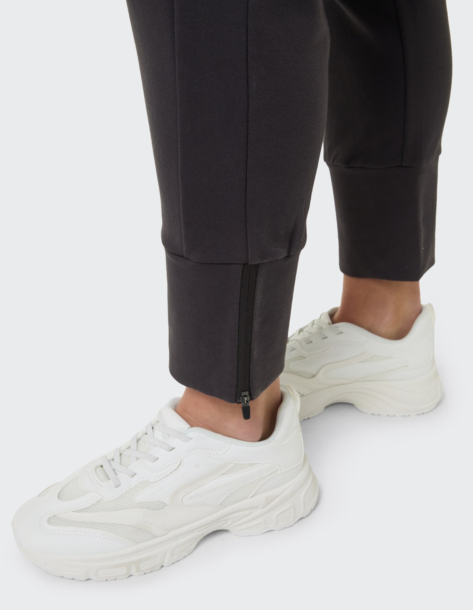 Nahaufnahme einer schwarzen Jogginghose mit Reißverschlussbündchen und weißen Turnschuhen für Freizeitkleidung.