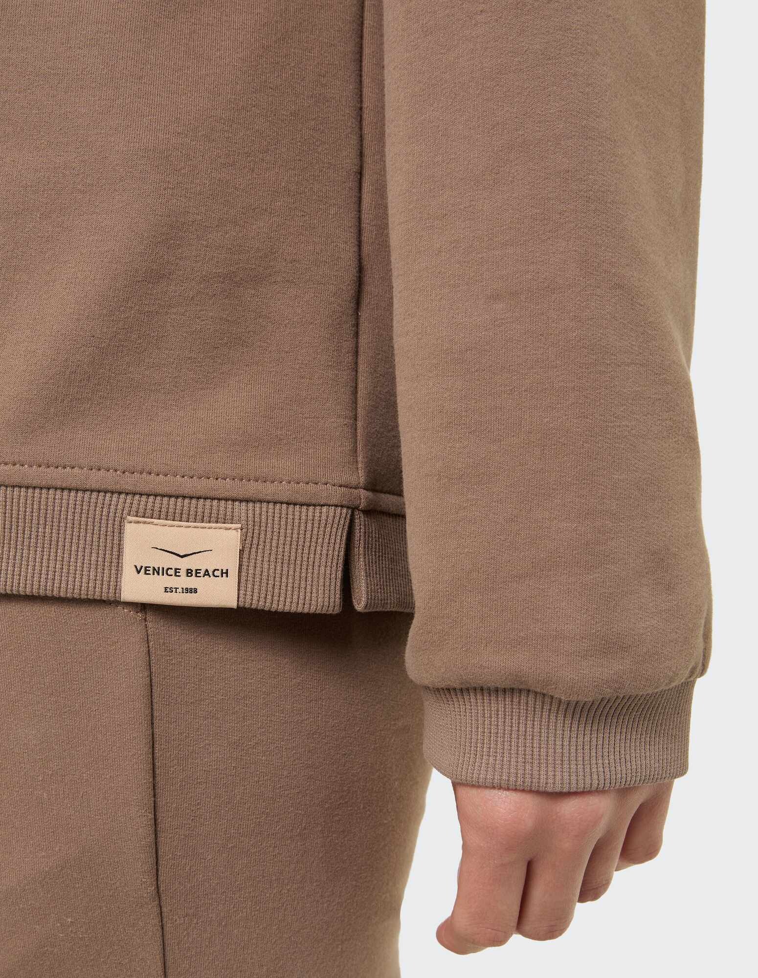Nahaufnahme eines gemütlichen braunen Sweatshirts mit gerippten Bündchen und Venice Beach-Etikett.
