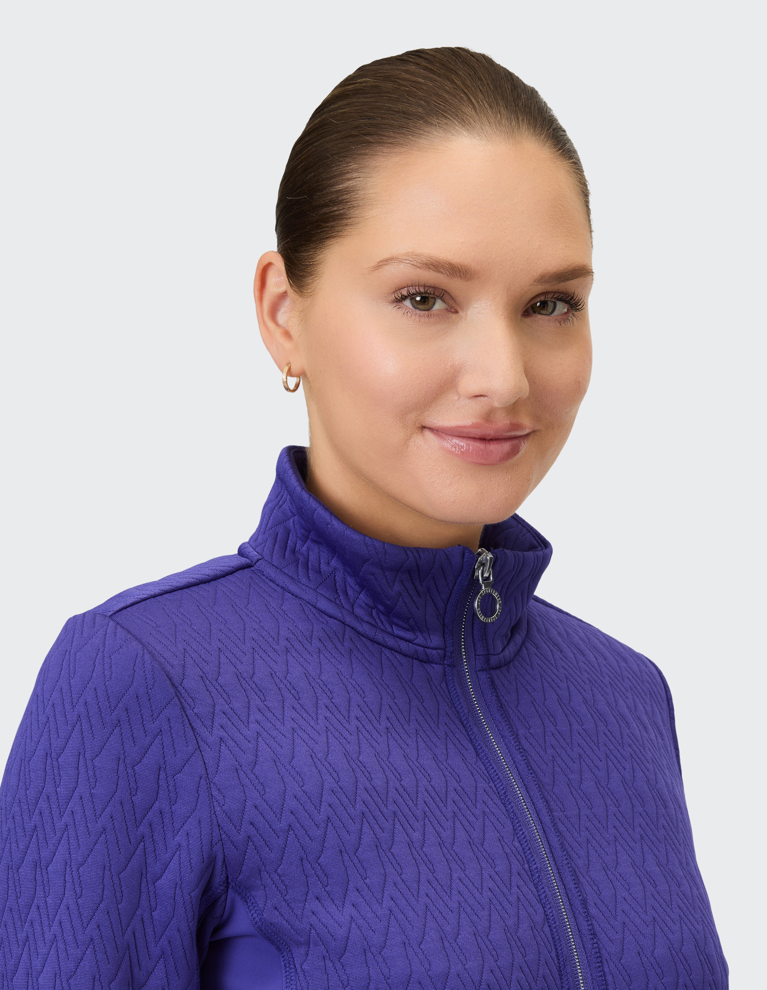 Eine Frau trägt eine violette Trainingsjacke mit durchgehendem Reißverschluss und einem auffälligen geometrischen Muster.