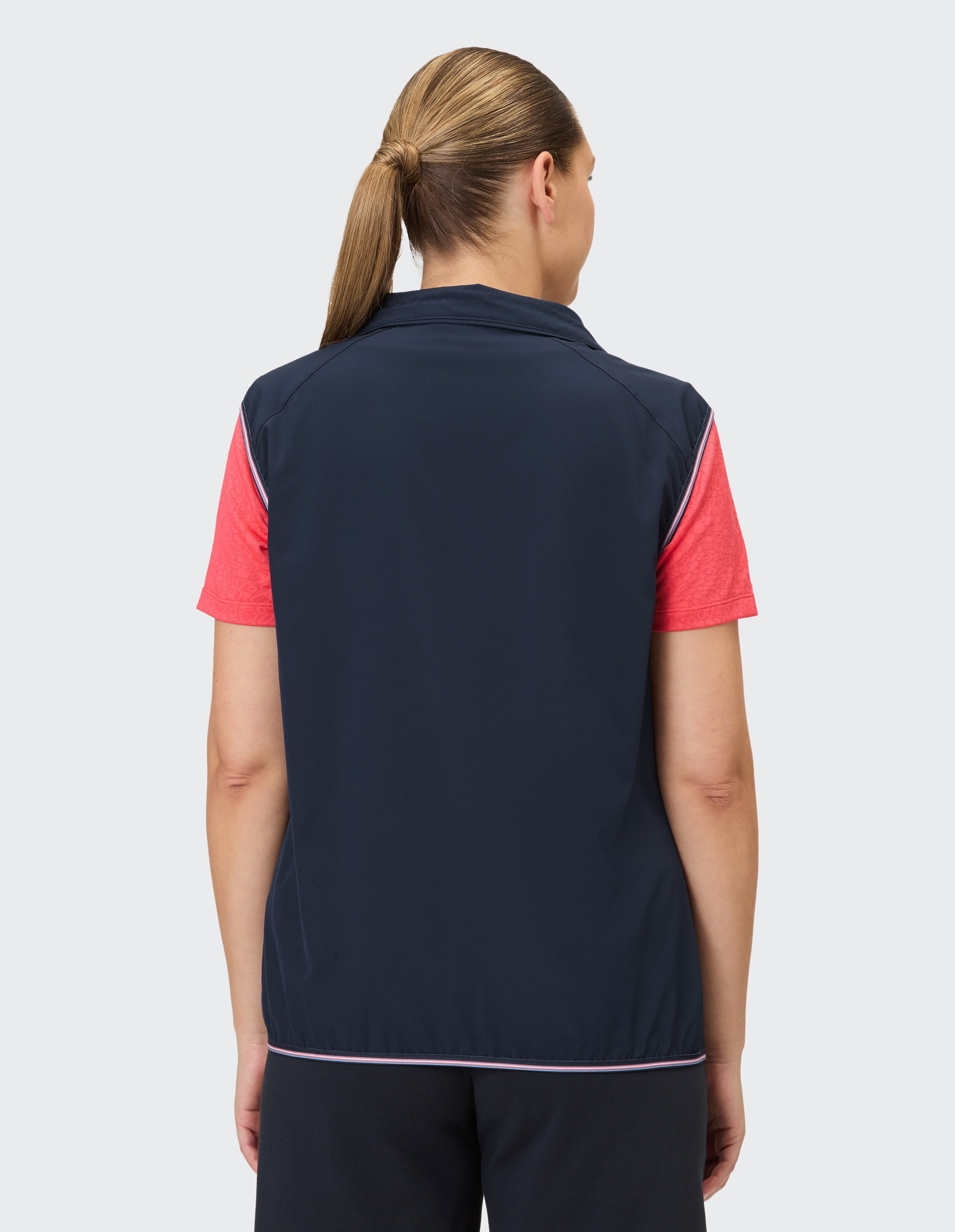 Rückansicht einer Frau in einer dunkelblauen Weste über einem rosa Hemd, ideal für Freizeitkleidung.
