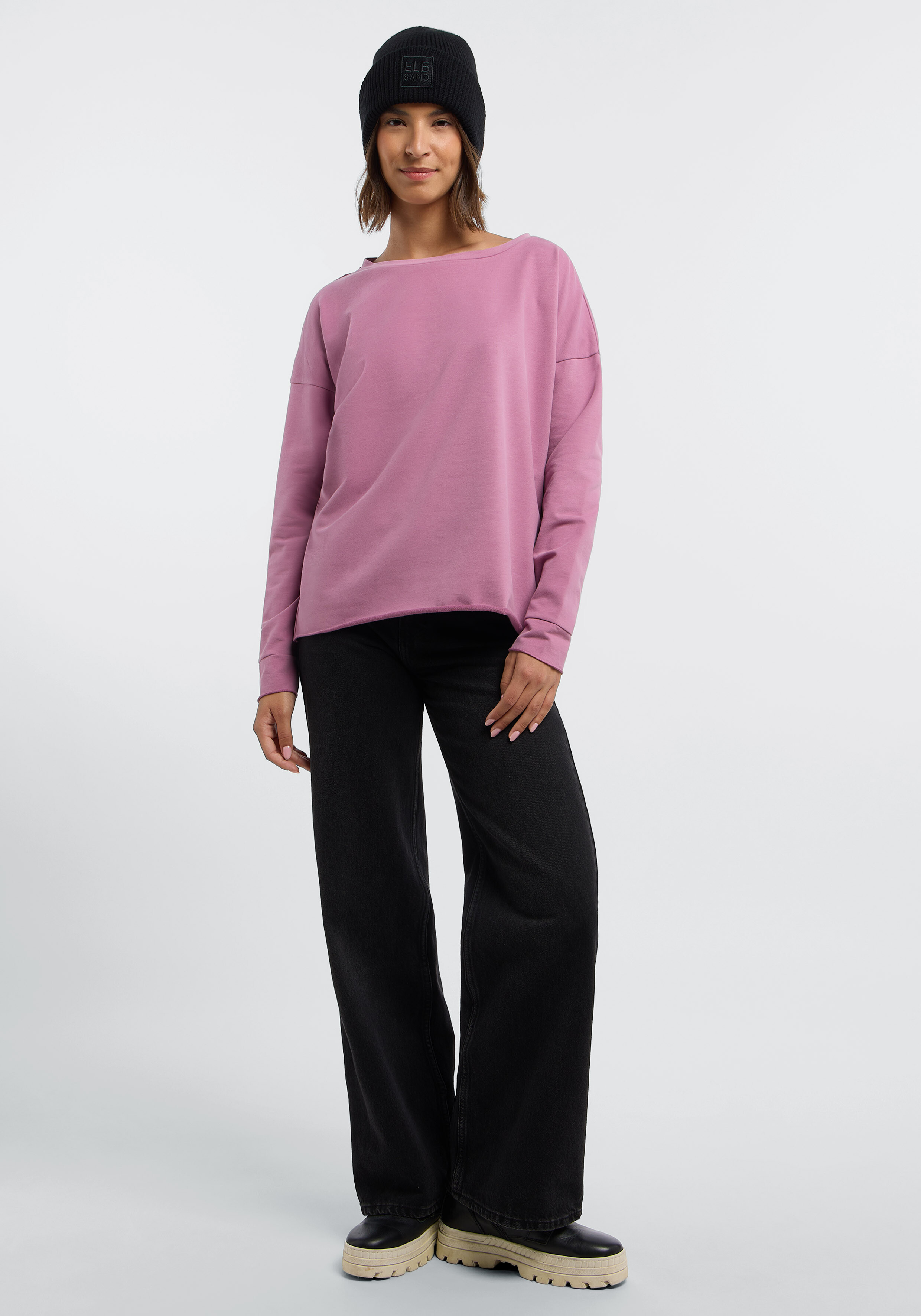Frau trägt einen rosa Langarmpullover, schwarze Jeans und eine schwarze Mütze für einen lässigen Stil.