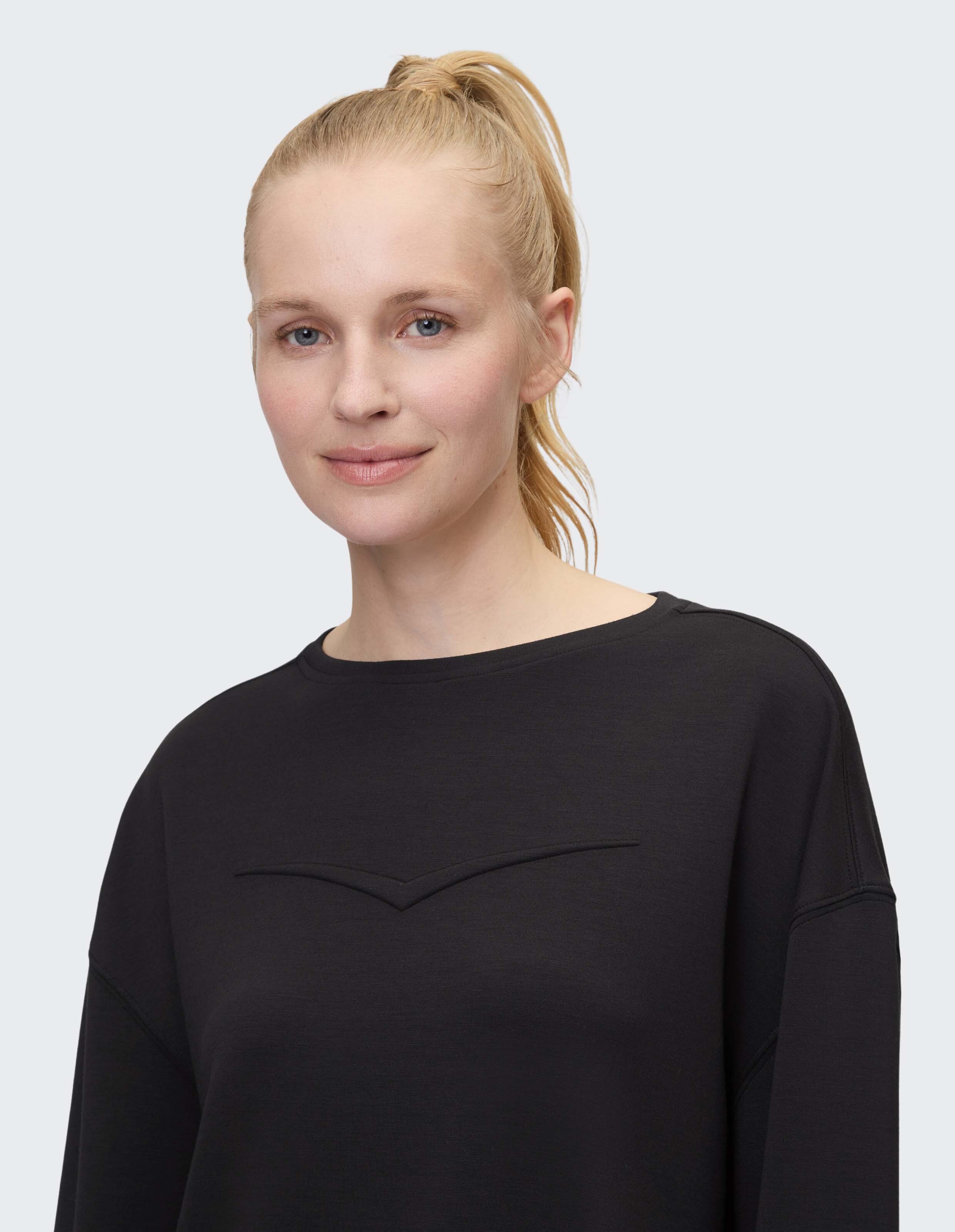 Nahaufnahme einer Frau in einem schwarzen, lässigen Sweatshirt mit stylischem Ausschnitt.