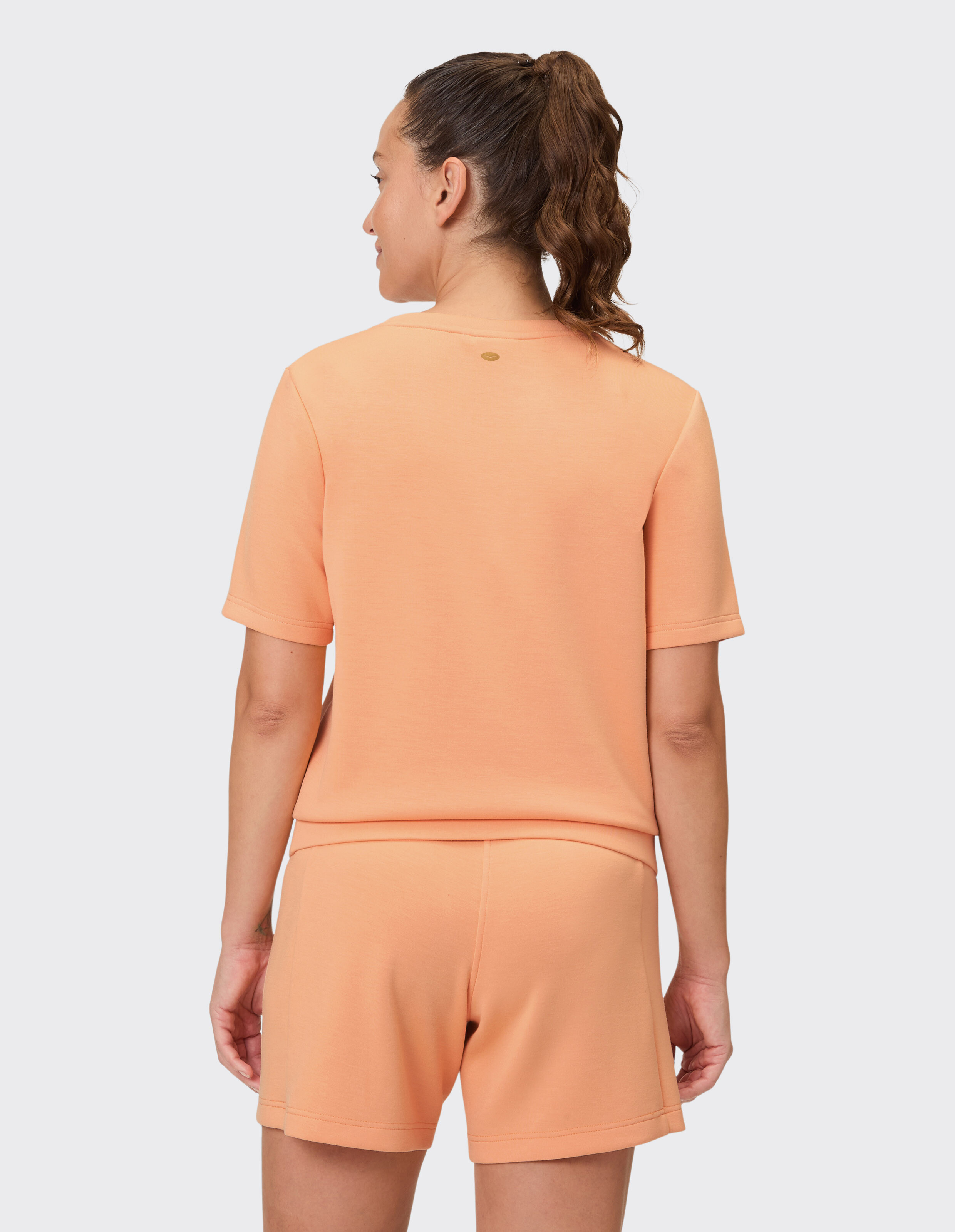 Rückansicht einer Frau in pfirsichfarbener Freizeitkleidung mit kurzärmeligem Oberteil und Shorts.
