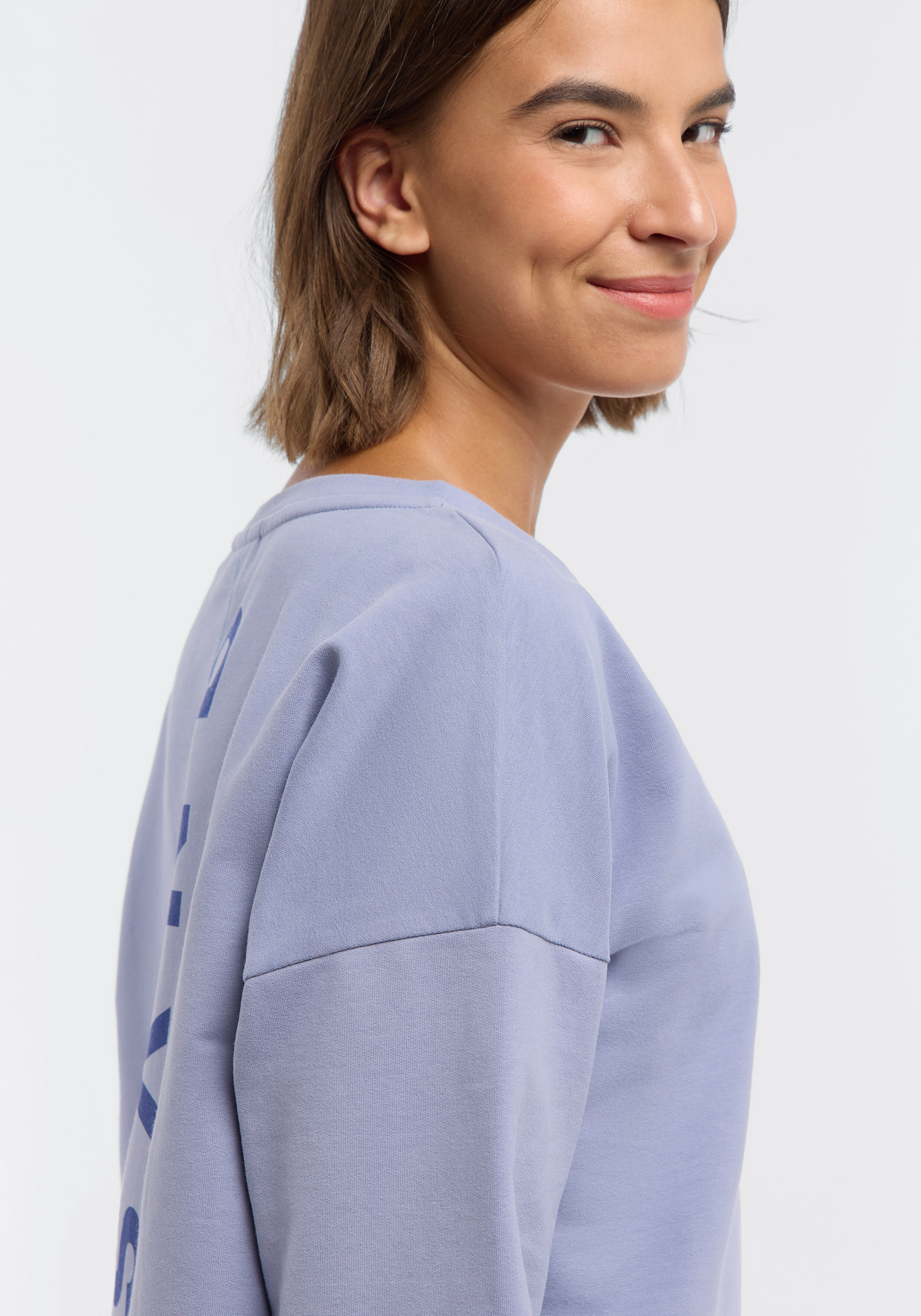 Frau trägt ein gemütliches hellviolettes Freizeit-Sweatshirt mit Logo-Detail.