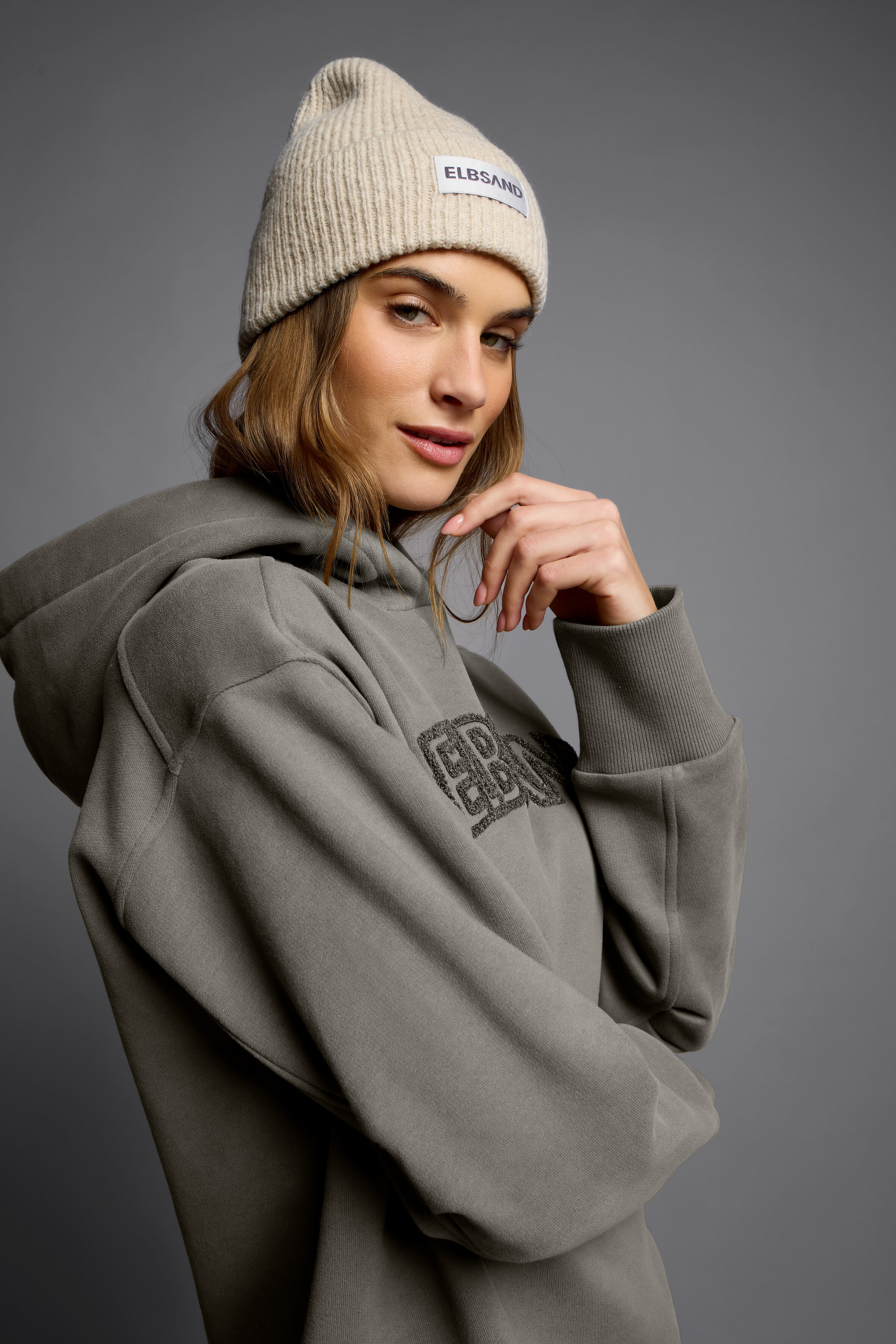 Frau trägt eine kuschelige beige Rippmütze und einen lässigen grauen ELBSAND-Hoodie.