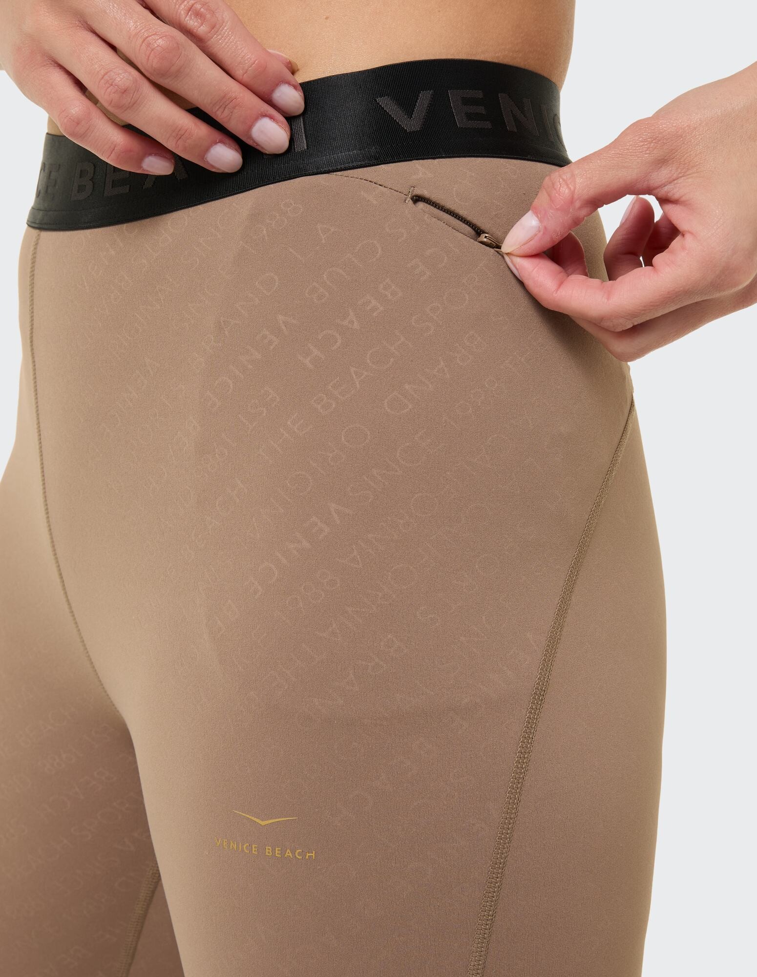Nahaufnahme einer beigen Leggings mit Logobund und Reißverschlusstaschendetail.