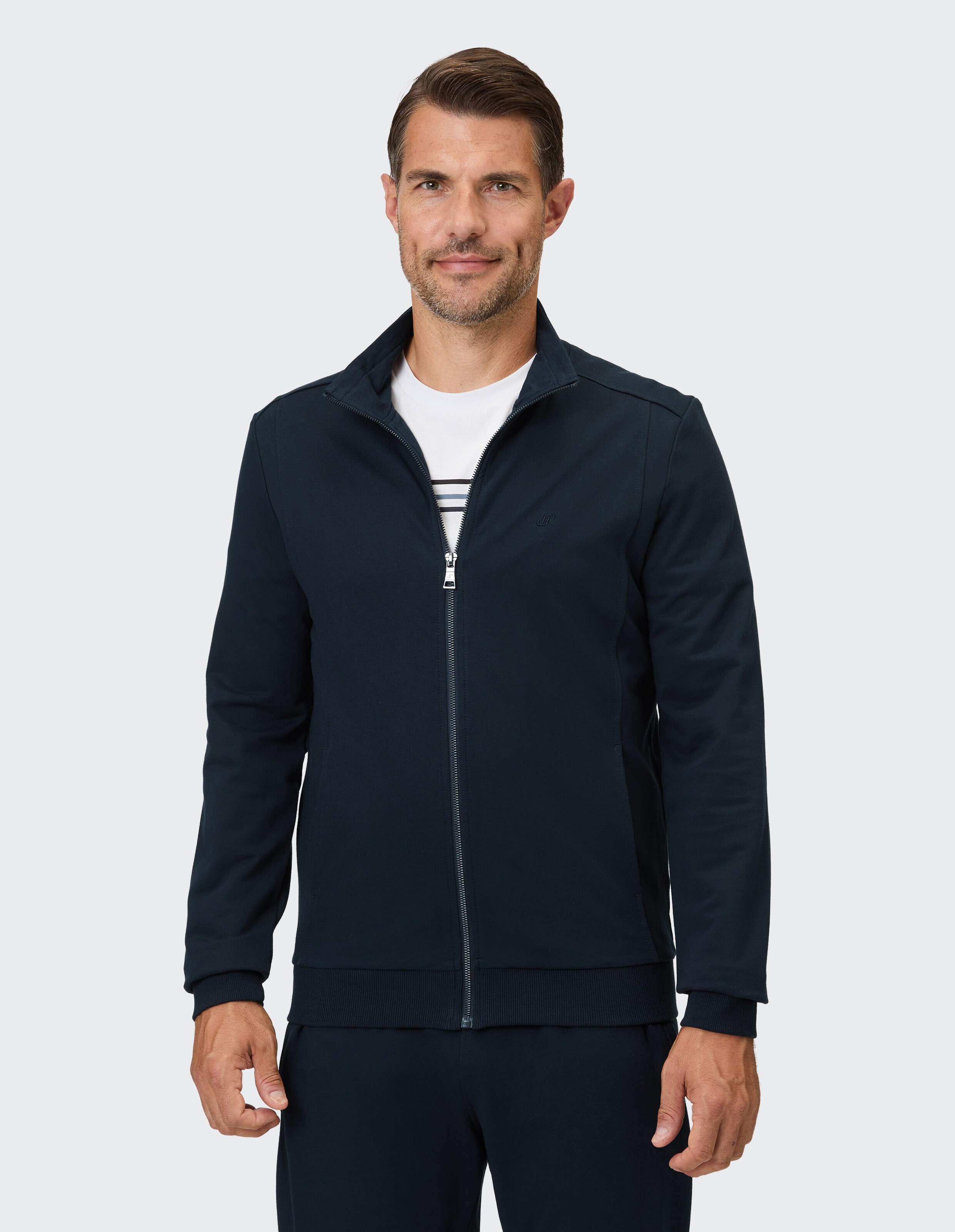 Mann trägt eine dunkelblaue Trainingsjacke mit durchgehendem Reißverschluss und Stehkragen.