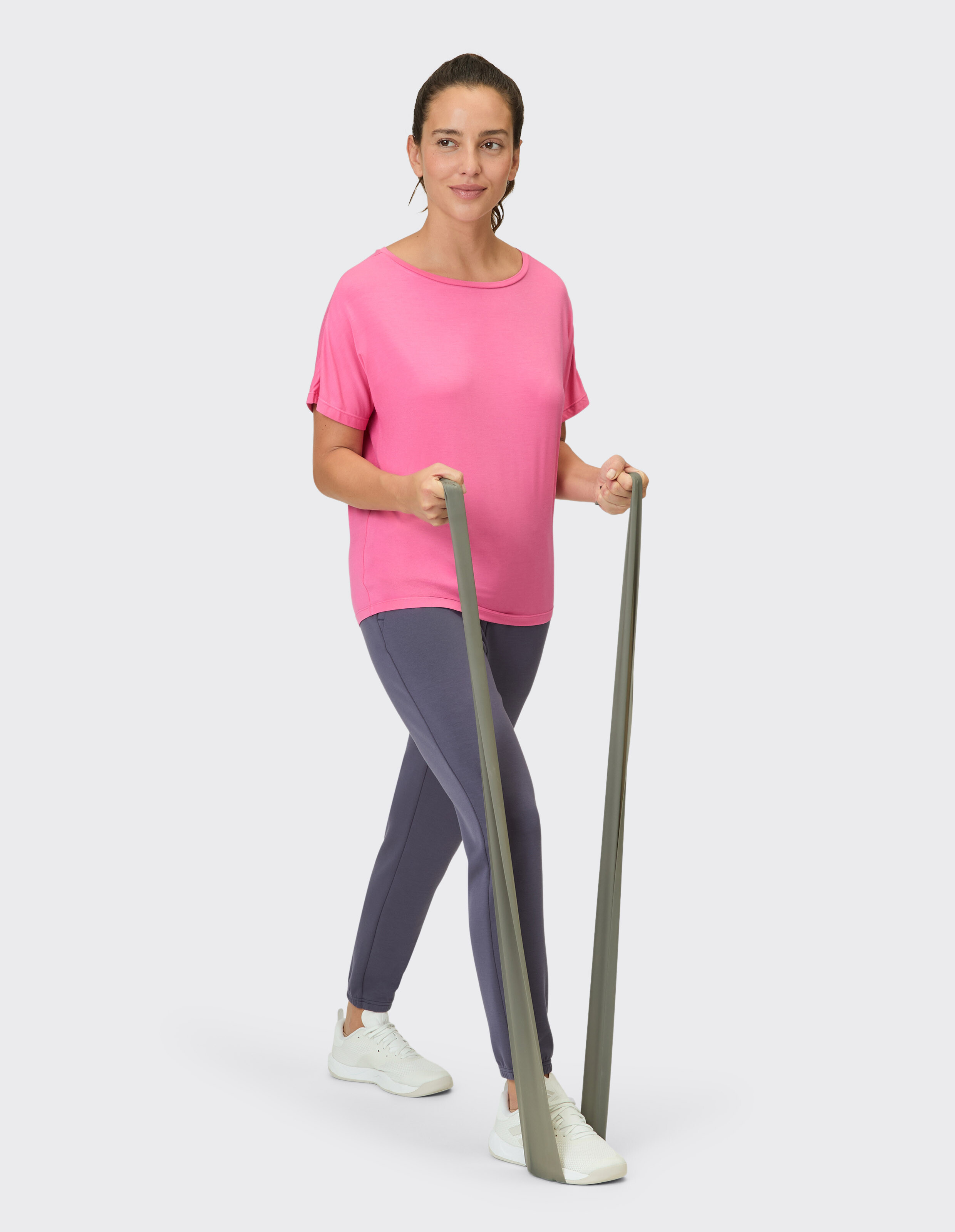 Frau in rosa Top und grauen Leggings trainiert mit Widerstandsbändern.