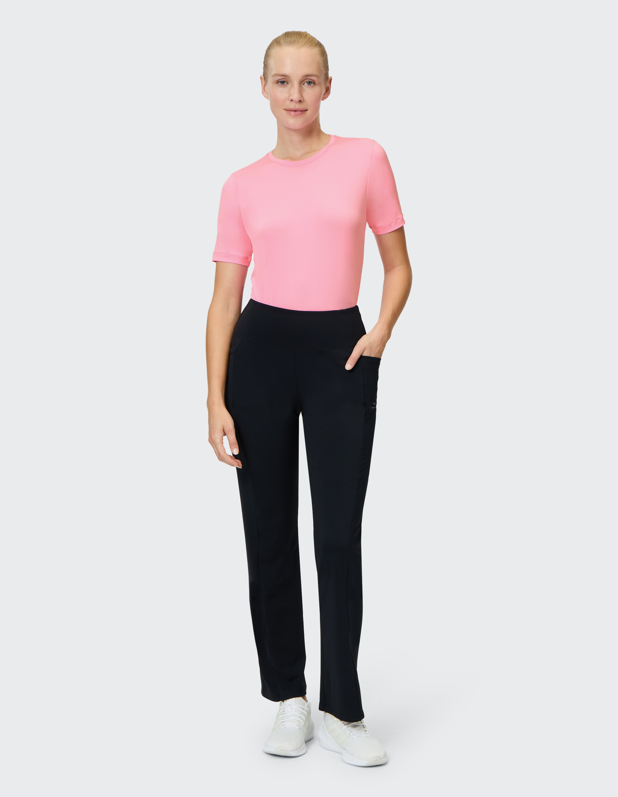 Frau in einem rosa Kurzarm-Top und einer schwarzen Hose, die einen lässigen Kleidungsstil präsentiert.
