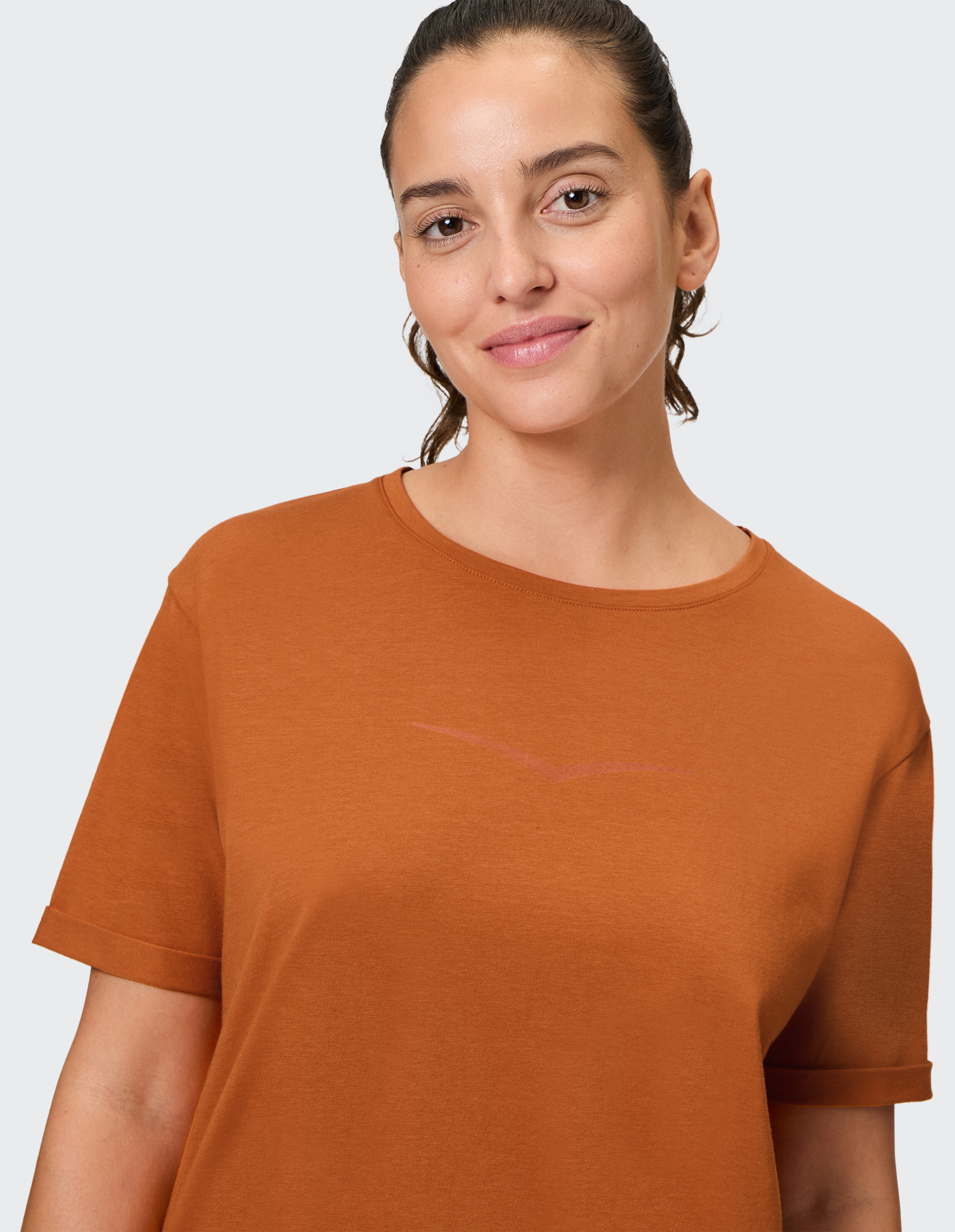 Frau trägt ein gemütliches, rostfarbenes Freizeit-T-Shirt mit aufgerollten Ärmeln.