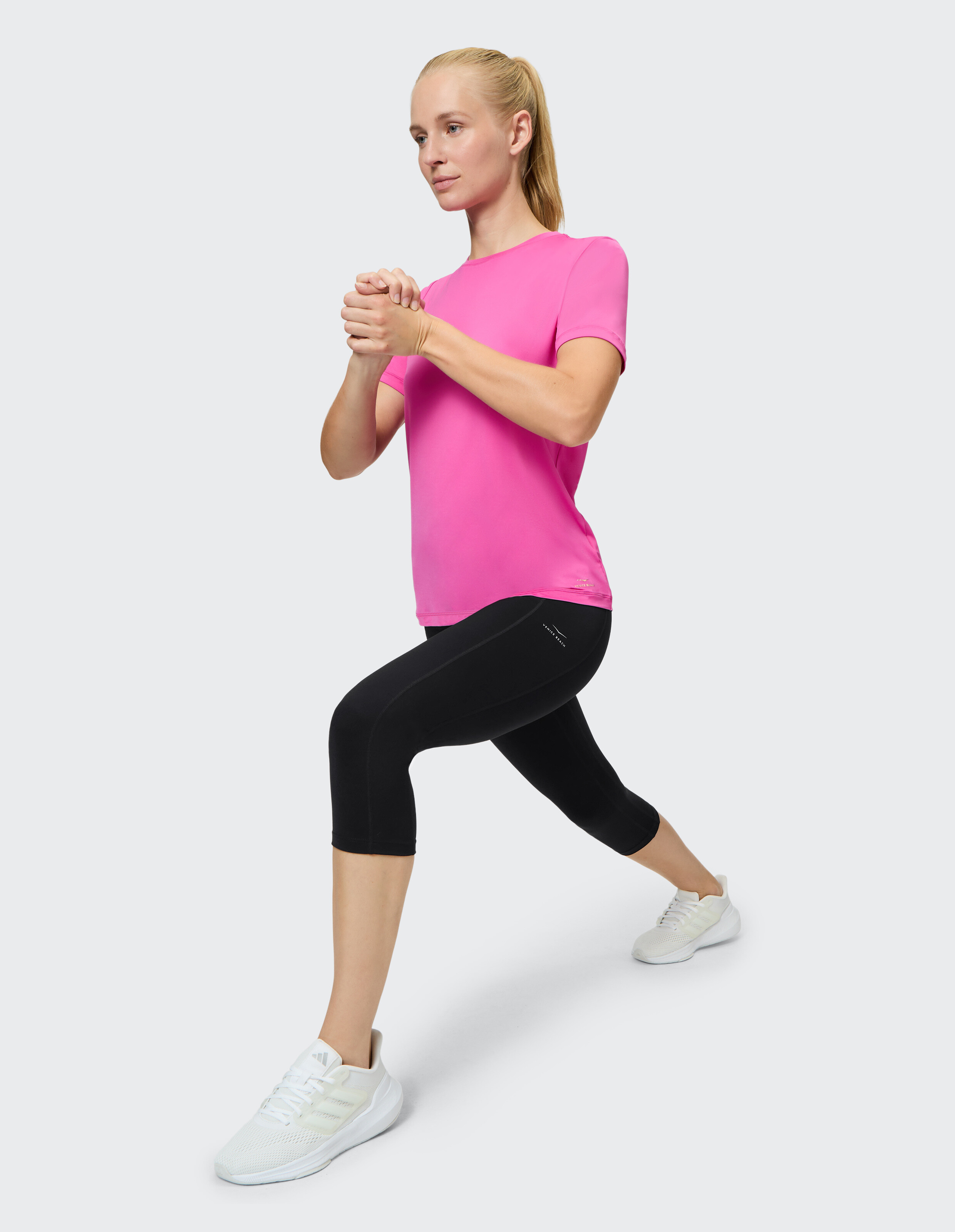 Frau in rosafarbenem Sportshirt und schwarzen Leggings macht einen Ausfallschritt.