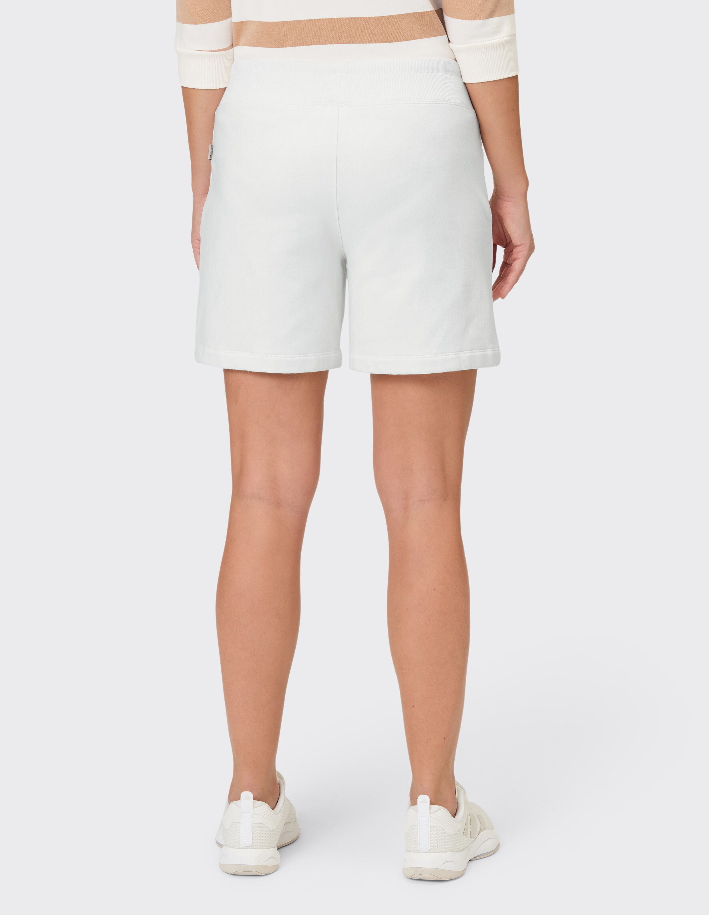 Rückansicht einer weißen, lässigen Sweat-Shorts gepaart mit einem gestreiften Oberteil und Turnschuhen.