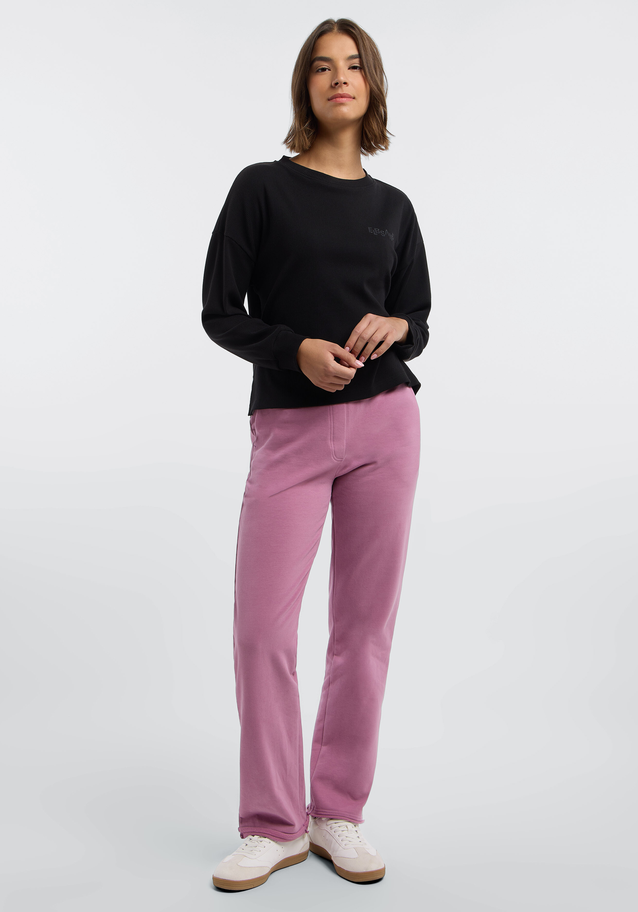 Frau trägt ein schwarzes Langarm-Sweatshirt und eine rosa Freizeithose.