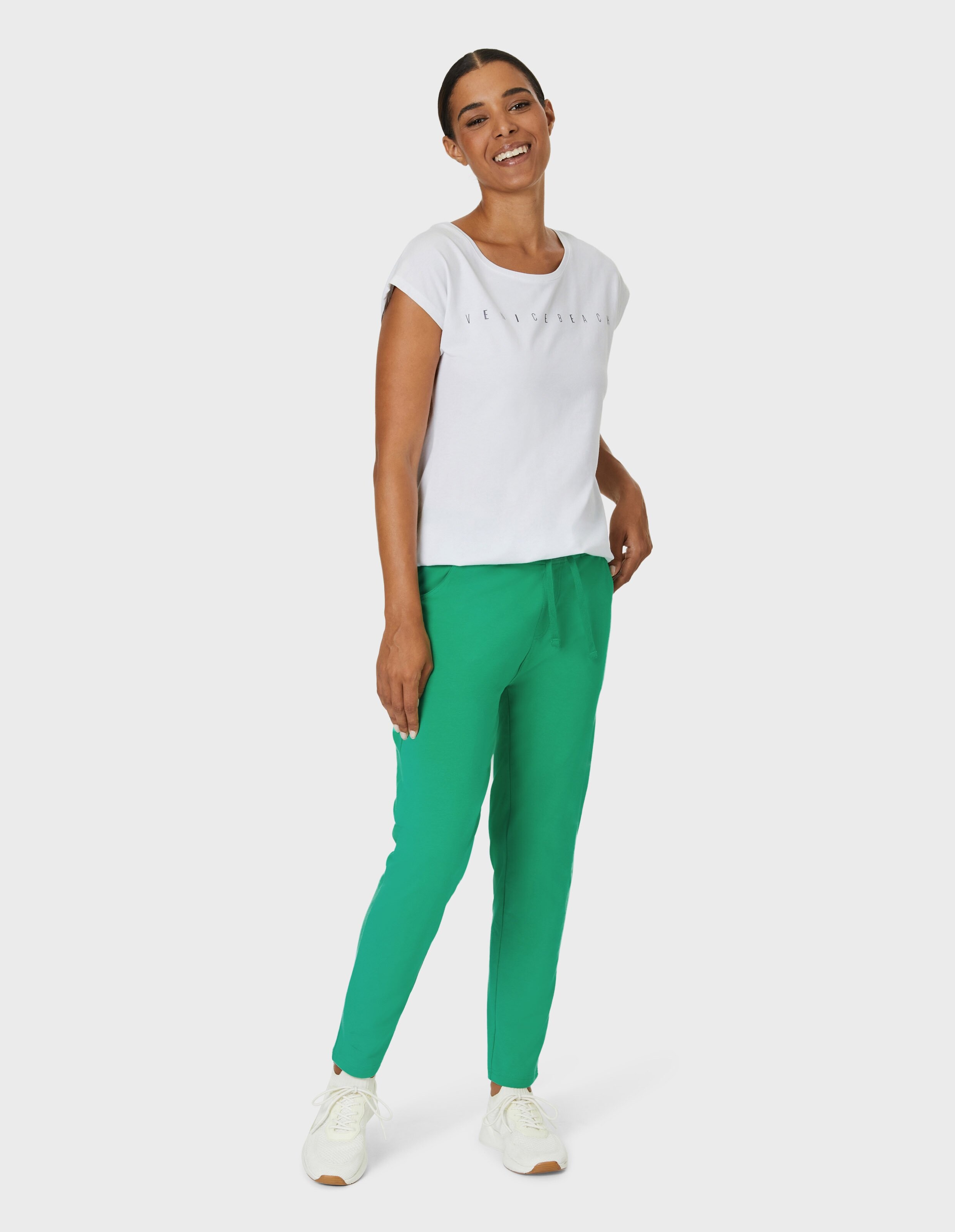 Frau trägt ein weißes T-Shirt und eine grüne Freizeithose für einen bequemen, stilvollen Look.