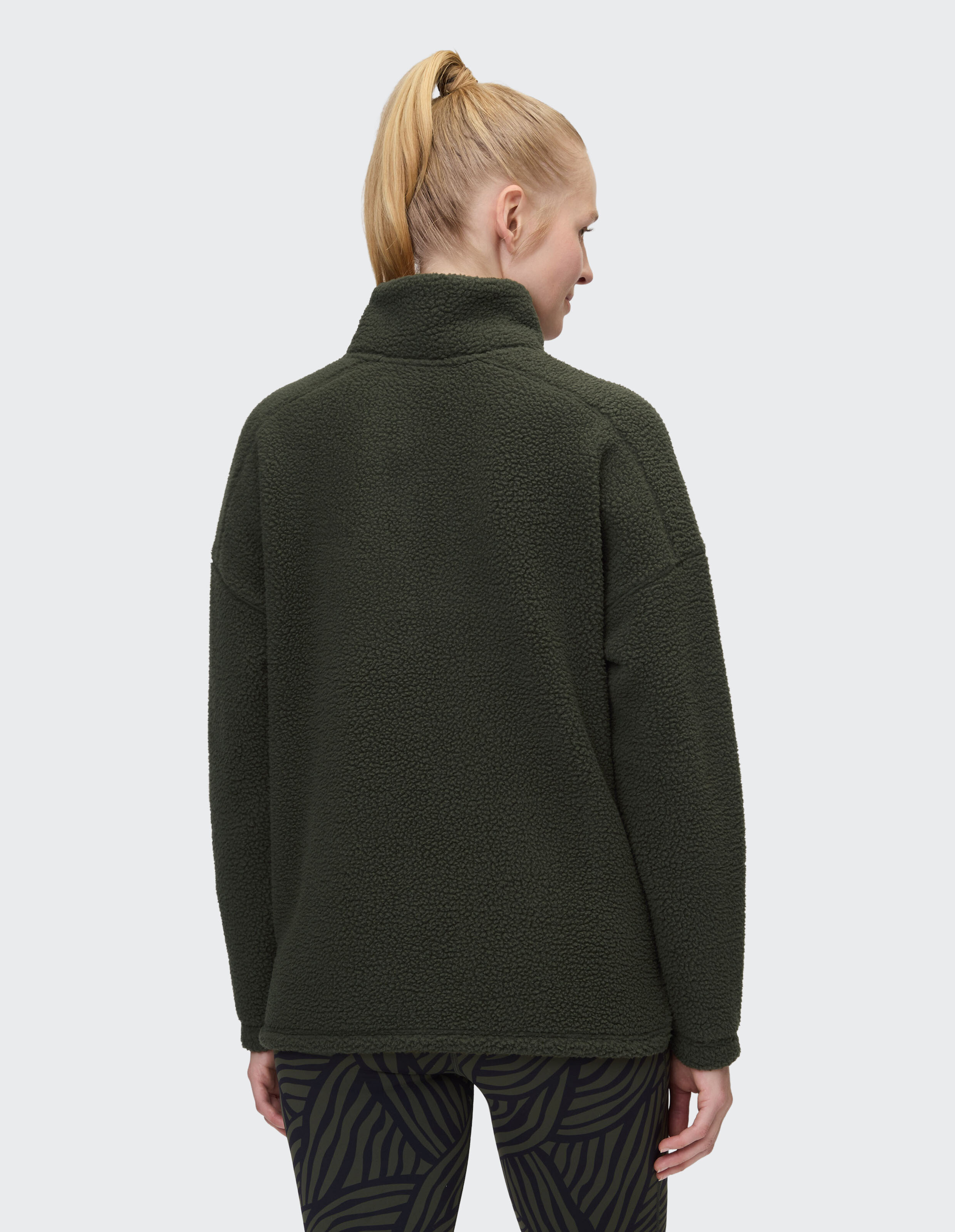 Frau trägt einen kuscheligen dunkelgrünen Teddyfleece-Pullover mit hohem Kragen, Rückansicht.