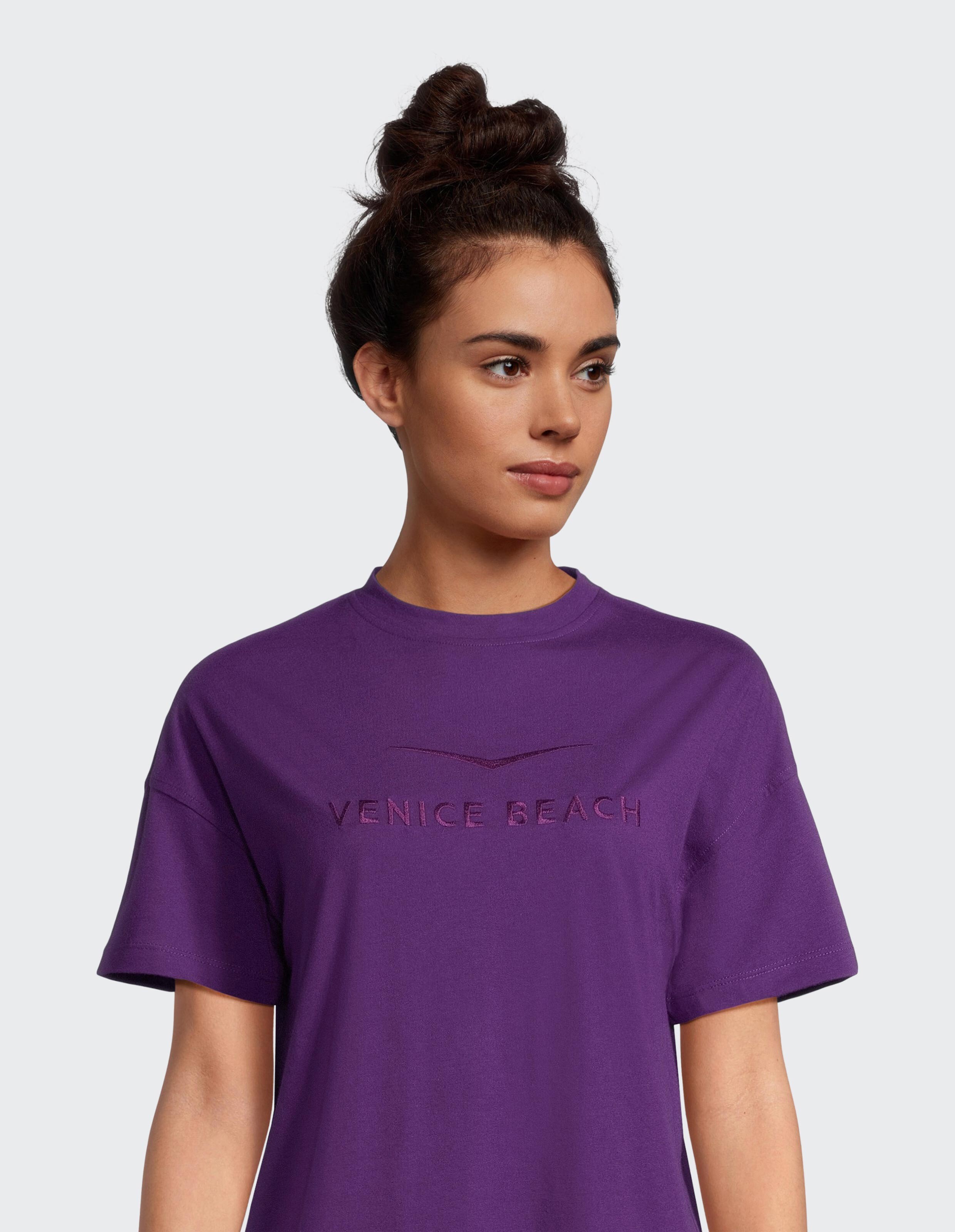 Das Model trägt ein lila T-Shirt mit „VENICE BEACH“-Logo im lässigen Stil.