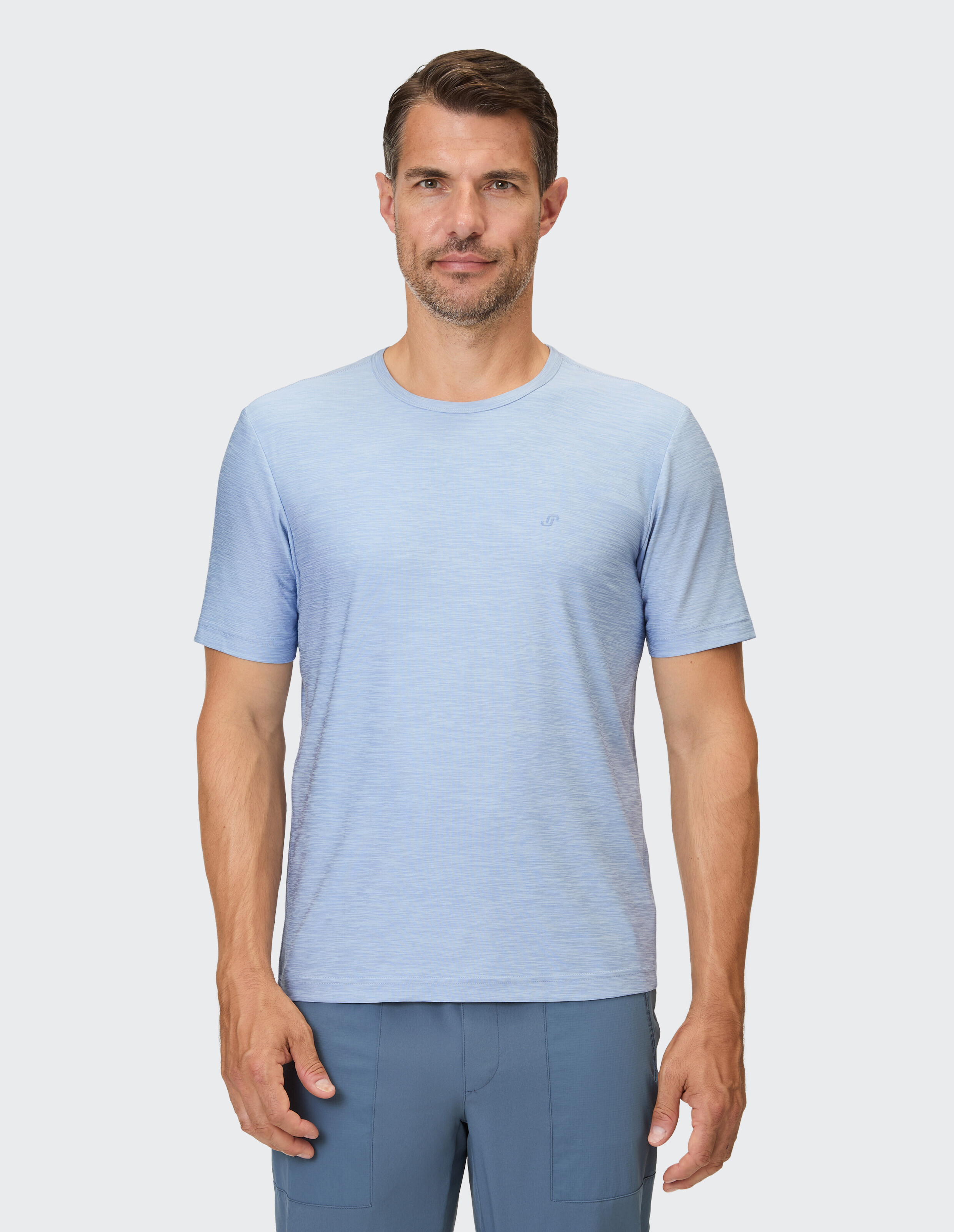 Ein Mann trägt ein hellblaues, kurzärmeliges Hemd mit feiner Struktur und ein dezentes Logo.