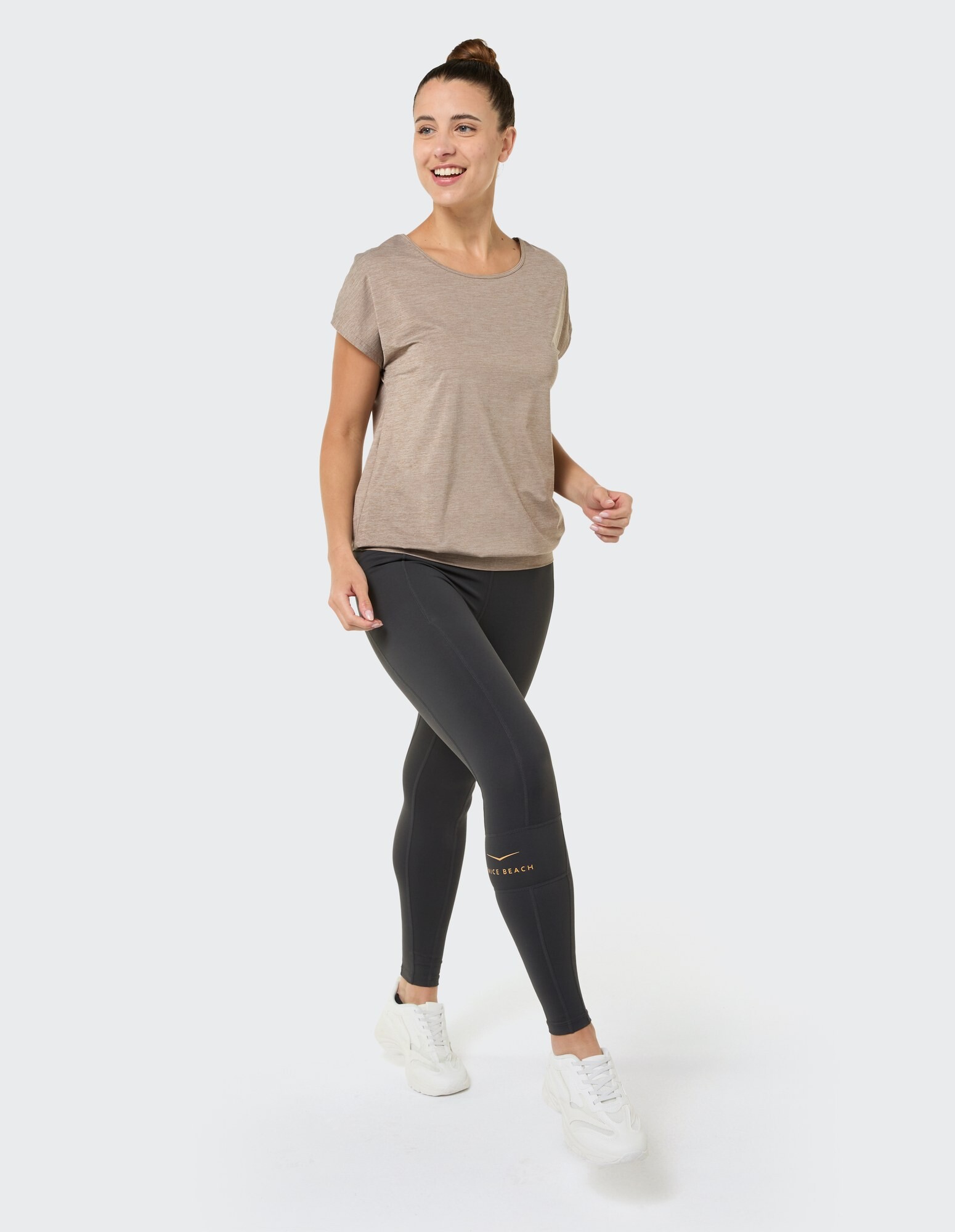 Frau in einem beigen Top und schwarzen Leggings, gestylt für lässigen Komfort.