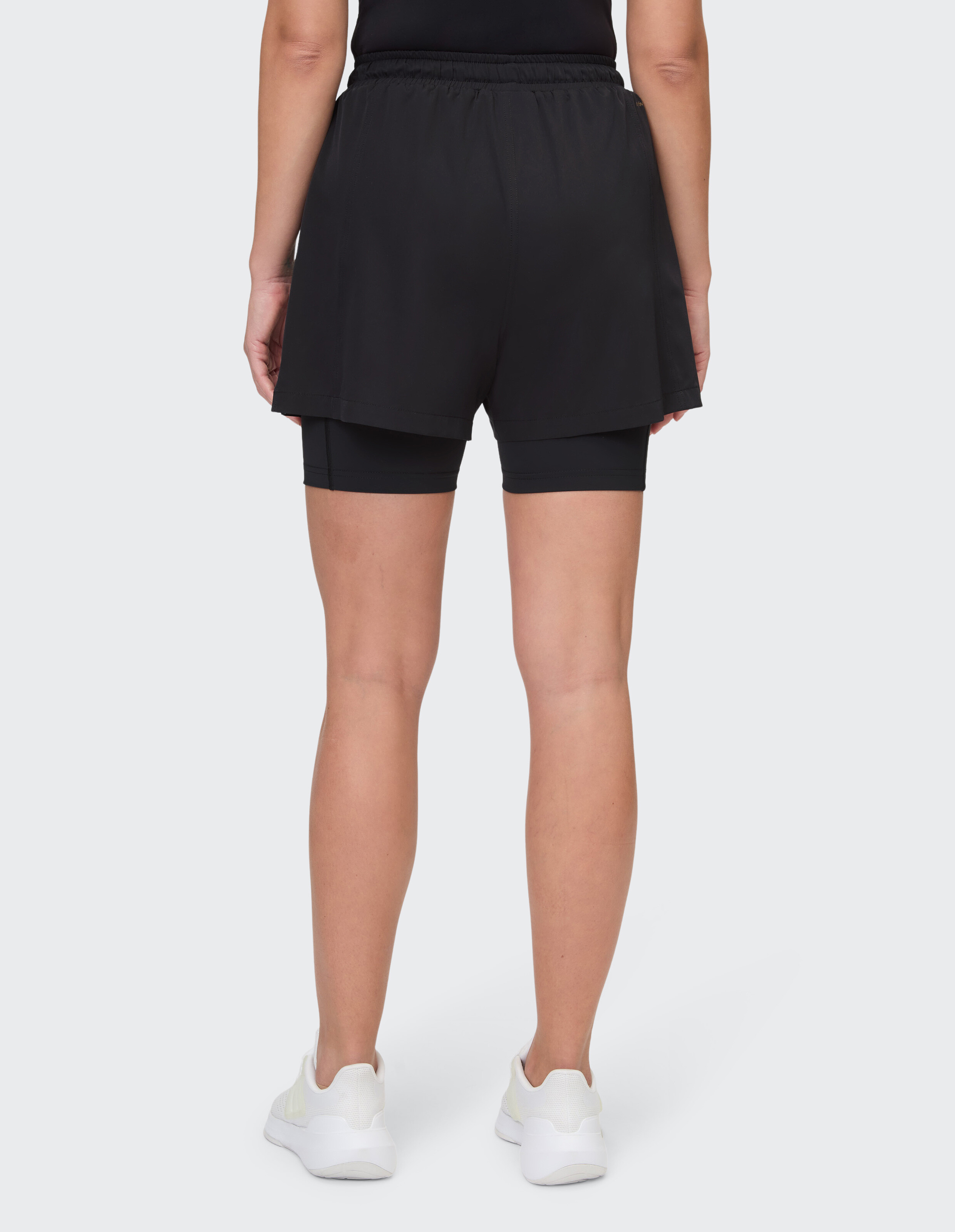 Rückansicht einer schwarzen, mehrlagigen, lässigen Sportshorts für Damen auf weißem Hintergrund.